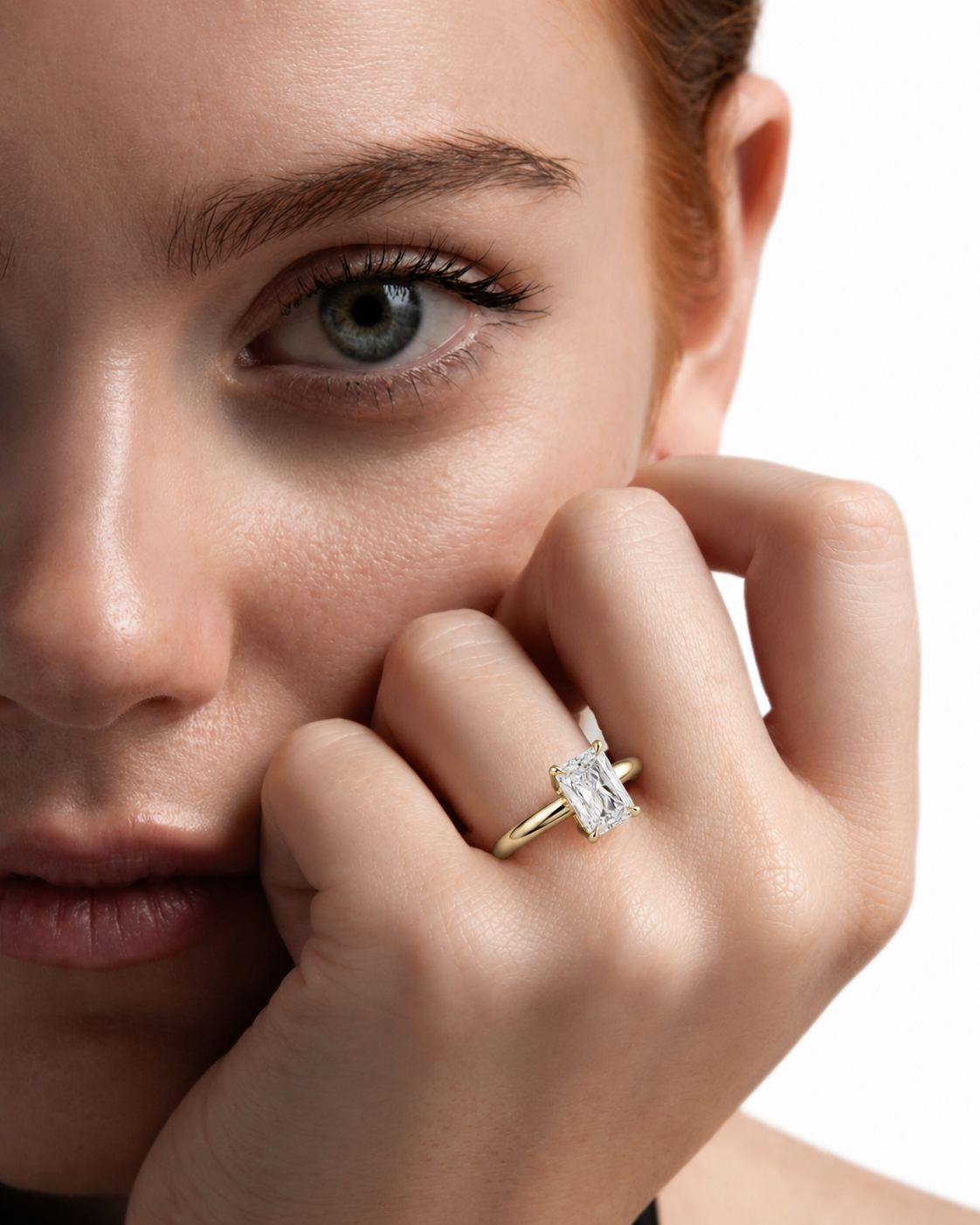 color_10K_YG, color_14K_YG &&A close-up lifestyle shot of a woman wearing a gold ring with a rectangular clear gemstone on her finger, with her face and hand prominently featured against a white background.