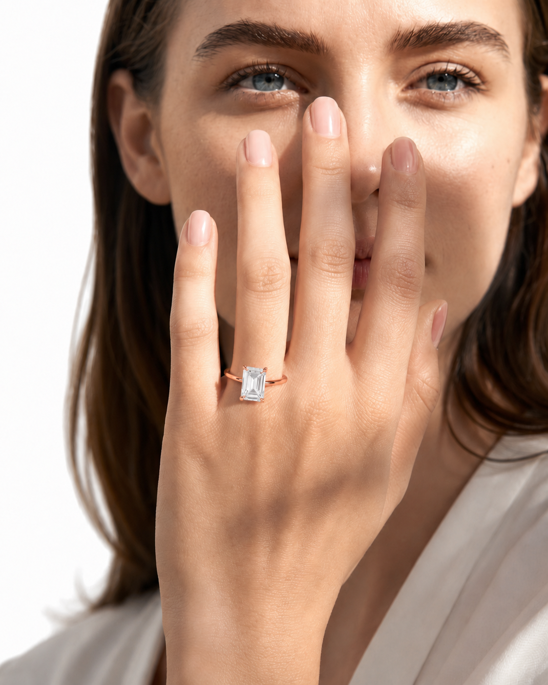 color_10K_RG, color_14K_RG &&
A close-up lifestyle shot of a woman wearing a rose gold ring with a rectangular baguette-cut clear gemstone on her ring finger, with her hand covering part of her face.