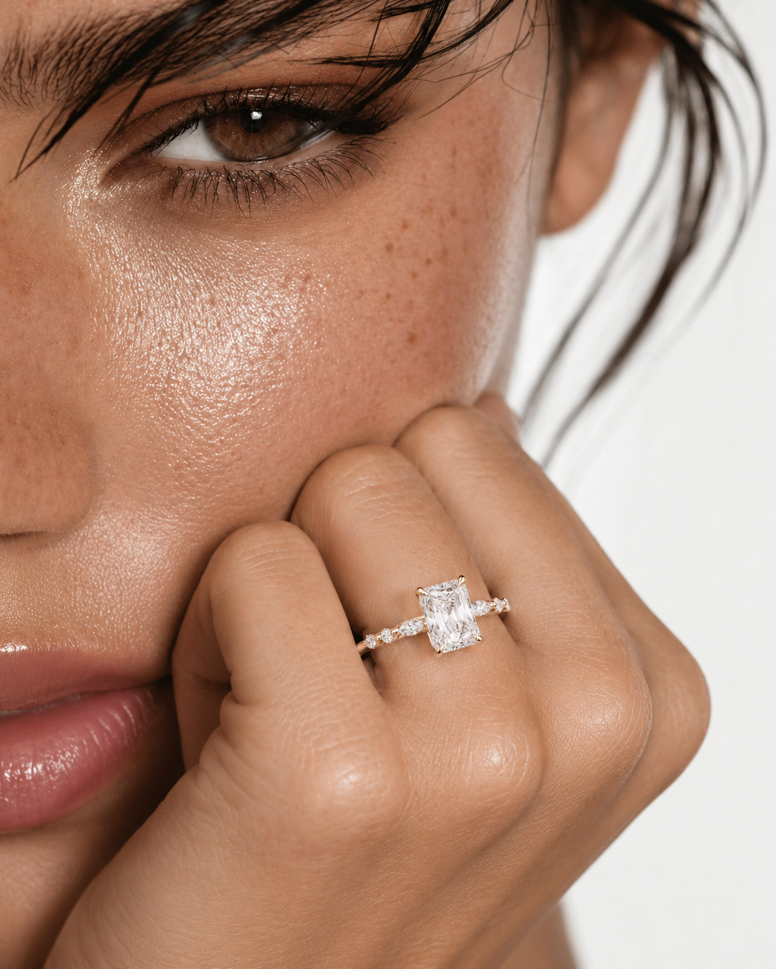 color_10K_YG, color_14K_YG &&A close-up lifestyle shot of a model wearing a diamond engagement ring with a rectangular emerald-cut center stone and a pavé band on her finger.
