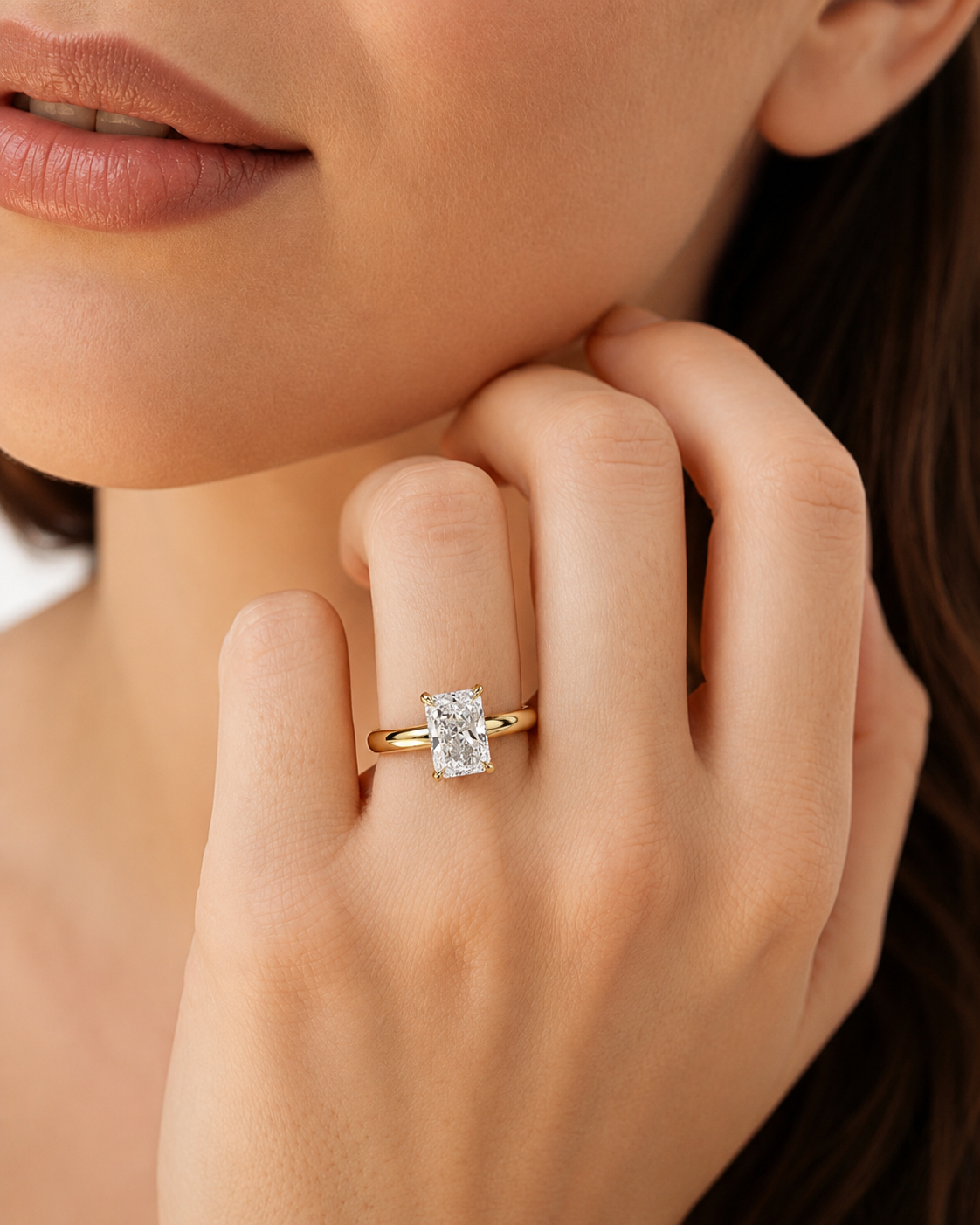 color_10K_YG, color_14K_YG &&A close-up lifestyle shot of a model wearing a yellow gold ring with a rectangular clear gemstone on her finger.