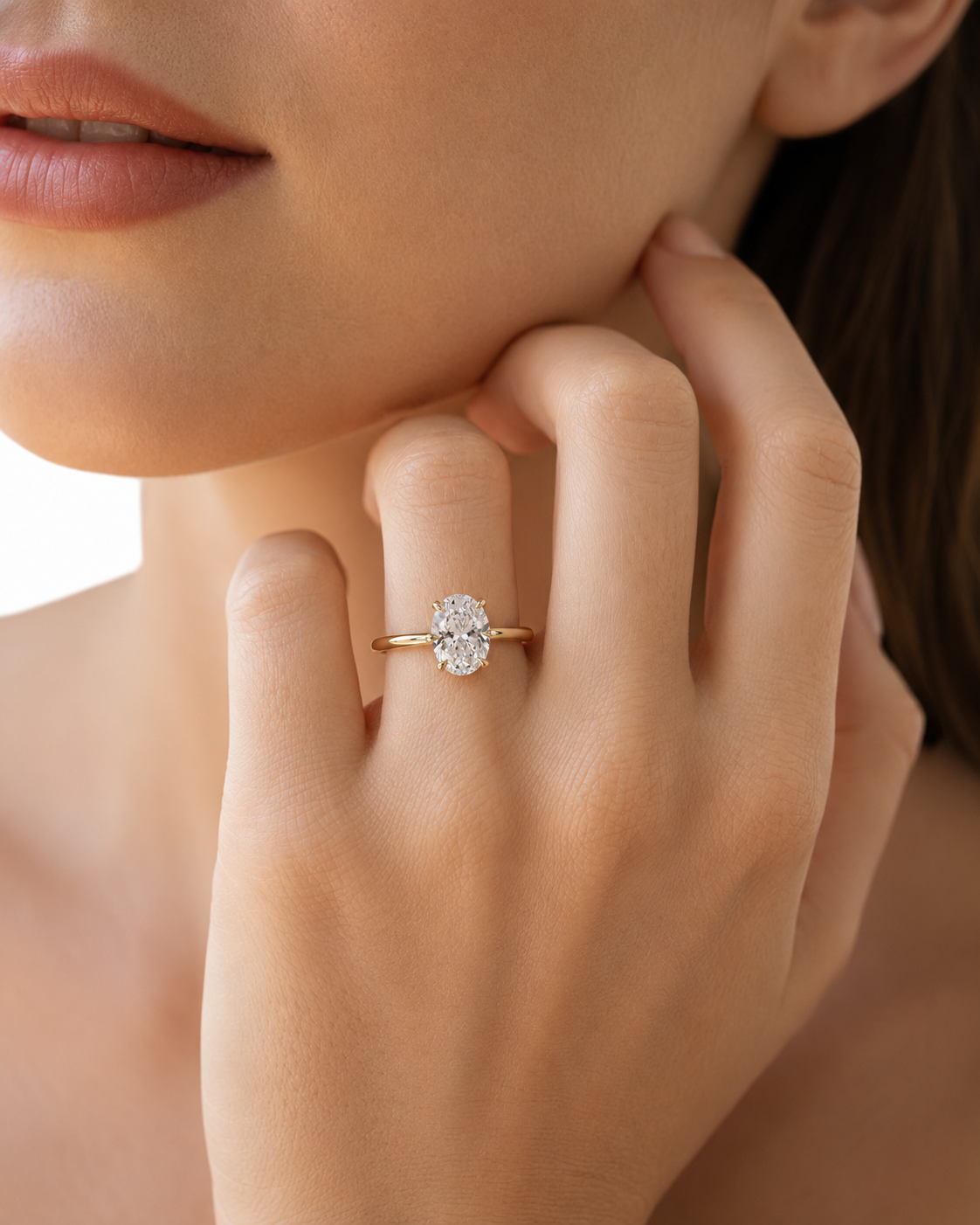 color_10K_YG, color_14K_YG &&A close-up lifestyle shot of a woman wearing a yellow gold ring with a round-cut diamond on her finger, with her hand resting near her chin.