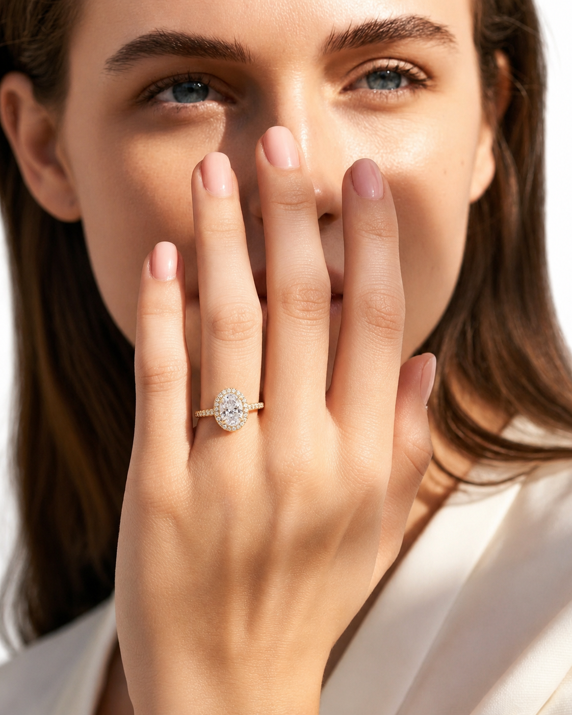 color_10K_YG, color_14K_YG &&A close-up lifestyle shot of a woman wearing a gold ring with a round-cut diamond halo on her finger, with her hand covering part of her face.