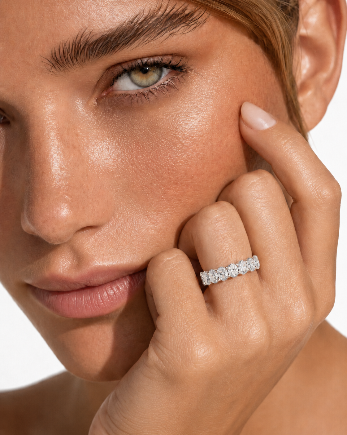 color_925_SIL,color_935_ARG,color_10K_WG, color_14K_WG &&	
A close-up lifestyle shot of a model wearing a delicate rose gold eternity ring set with small clear stones on her finger, with her hand resting against her cheek against a clean white background.