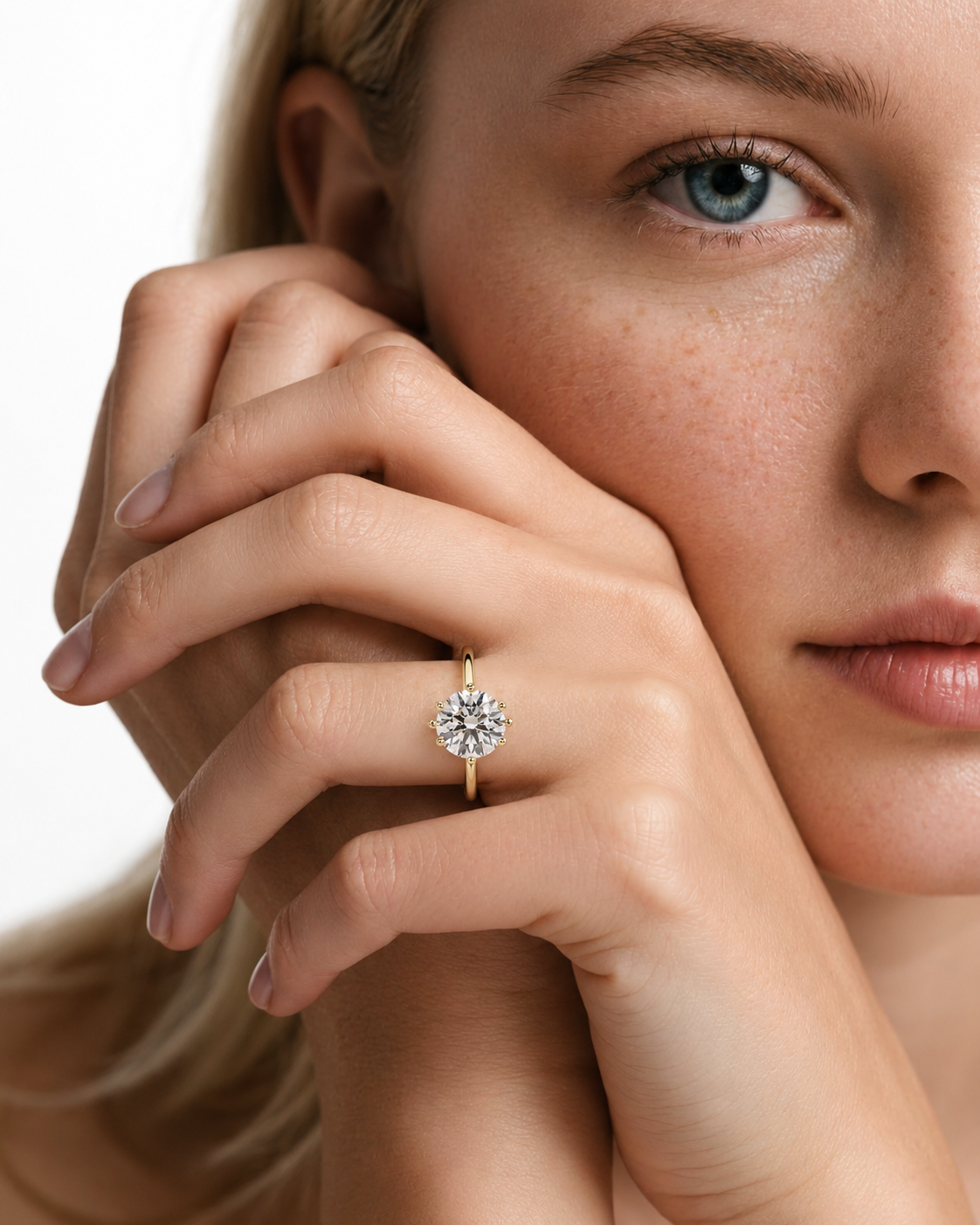 color_10K_YG, color_14K_YG &&A close-up lifestyle shot of a model wearing a yellow gold ring with a round-cut clear gemstone. The ring is shown on her finger, with her face and hand prominently featured against a clean white background.