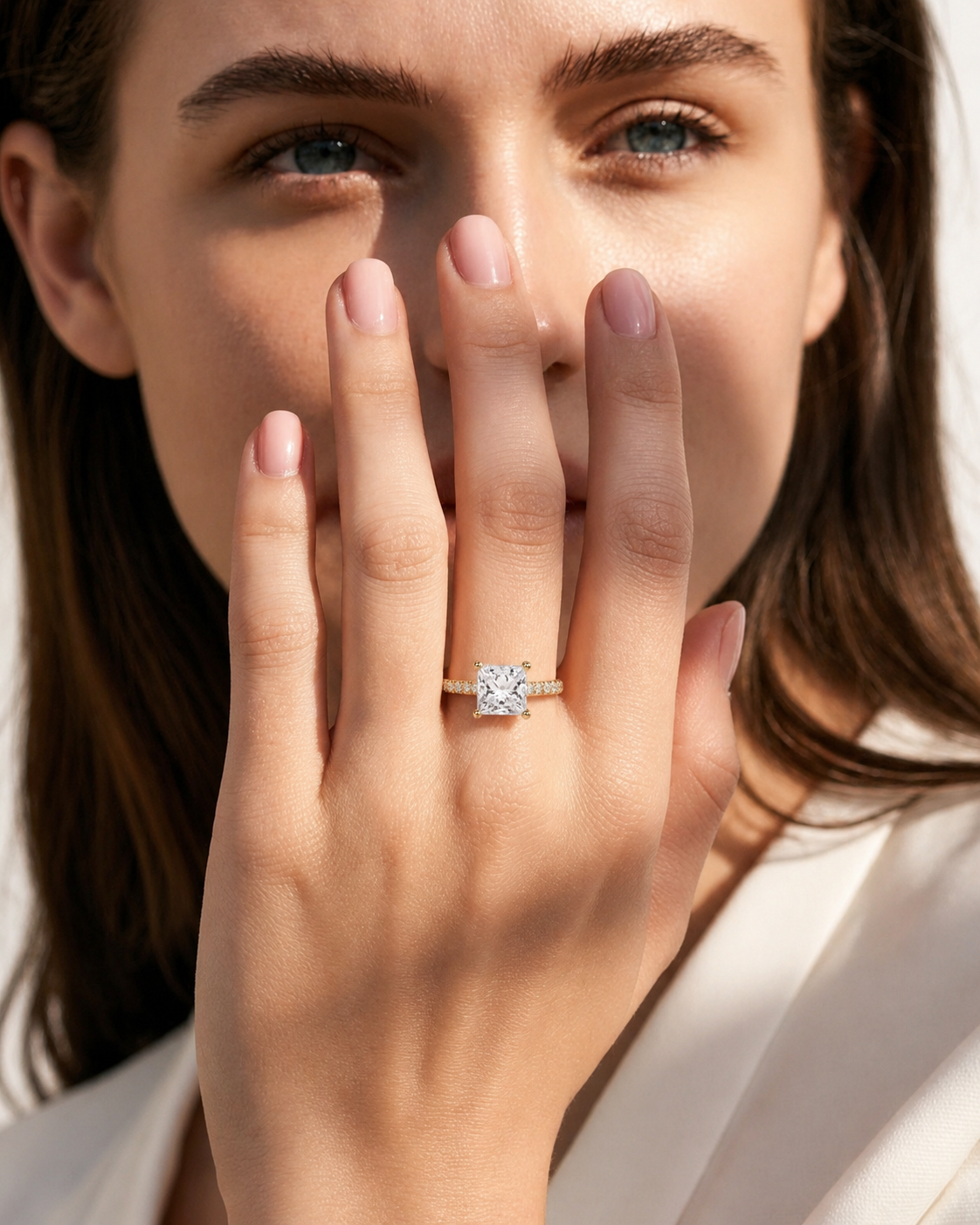 color_10K_YG, color_14K_YG &&A close-up lifestyle shot of a woman wearing a diamond engagement ring on her finger, holding her hand near her face. The ring features a round brilliant-cut diamond set in a yellow gold band.