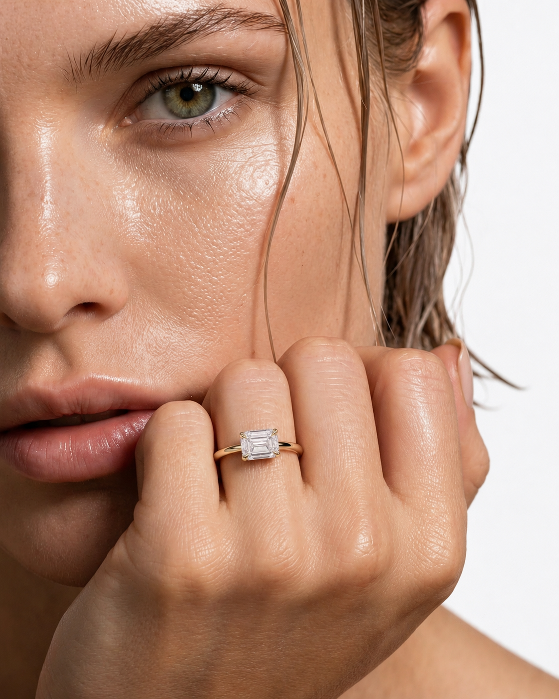 color_10K_YG, color_14K_YG &&A close-up lifestyle shot of a model wearing a gold engagement ring with an emerald-cut clear center stone on her finger.