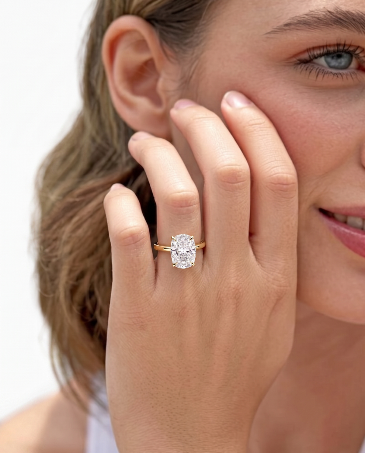 color_10K_YG, color_14K_YG &&A close-up lifestyle shot of a woman wearing a yellow gold ring with an oval-cut clear gemstone on her finger, set against a clean white background.