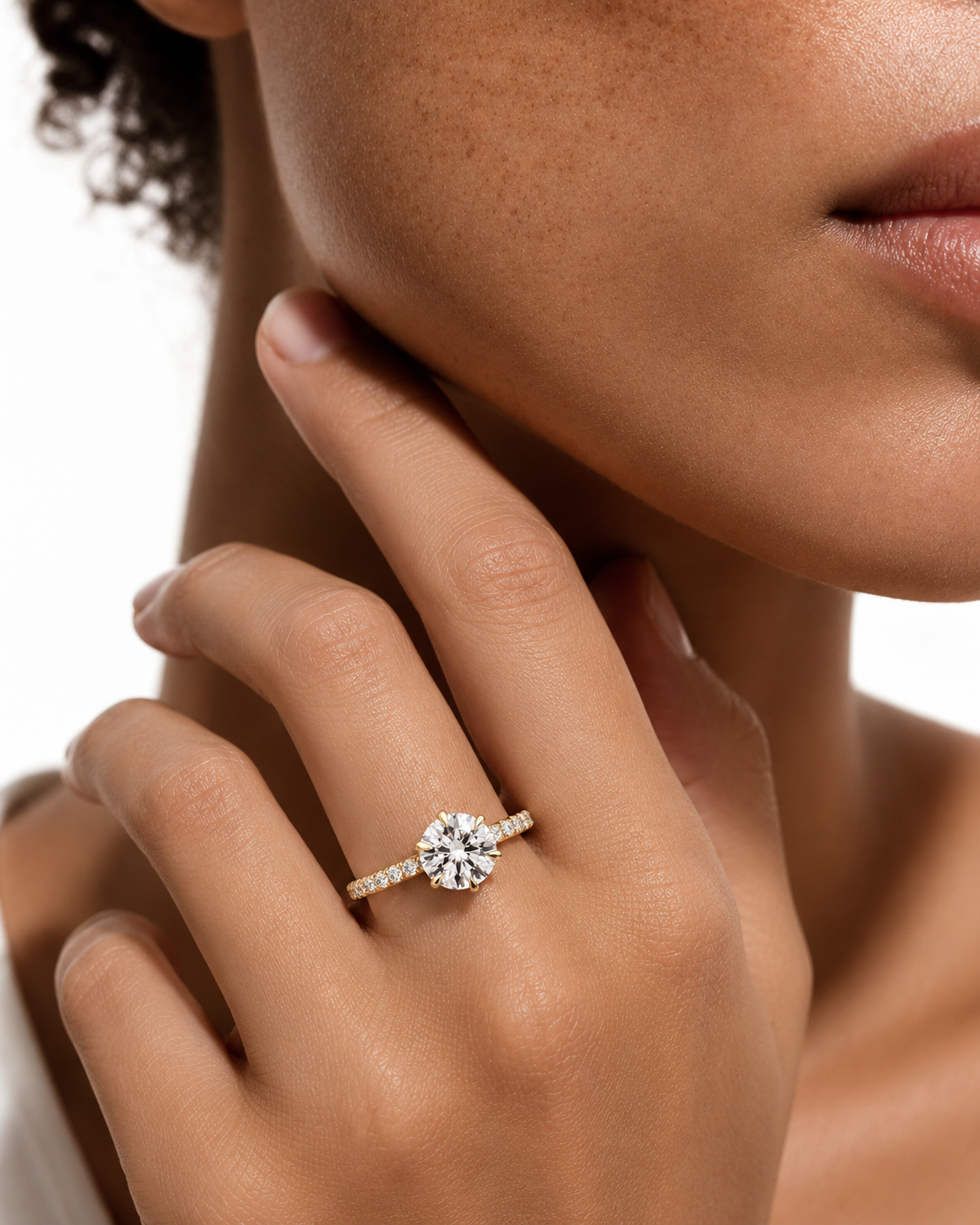 color_10K_YG, color_14K_YG &&
A close-up lifestyle shot of a model wearing a diamond engagement ring on her finger. The ring features a round brilliant-cut center stone set on a thin, pave-set band.