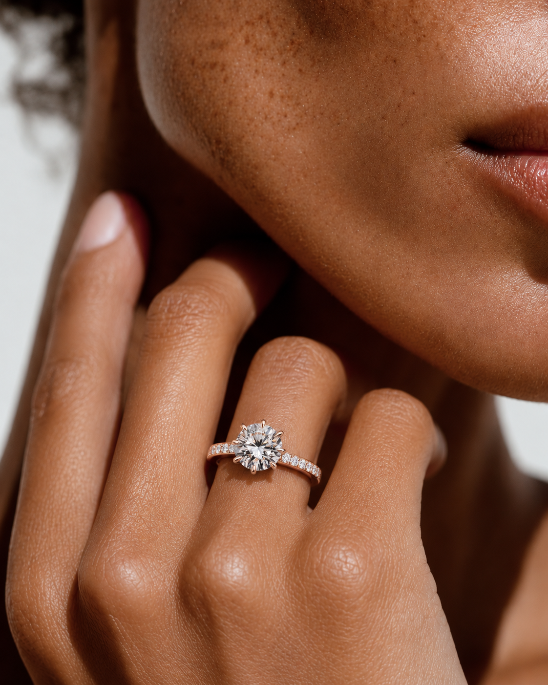 color_10K_RG, color_14K_RG &&
A close-up lifestyle shot of a model's hand wearing a sparkling diamond engagement ring with a rose gold band.
