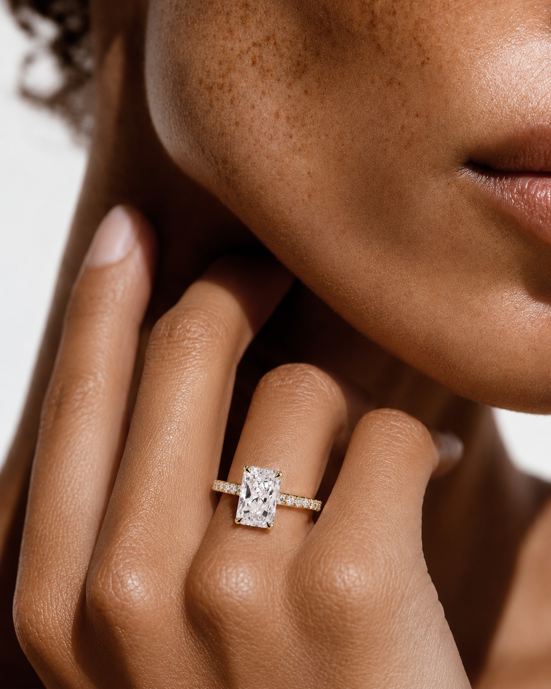 color_10K_YG, color_14K_YG &&A close-up lifestyle shot of a model wearing a diamond engagement ring with a rectangular baguette-cut center stone and a pavé band, shown on her finger against a clean white background.