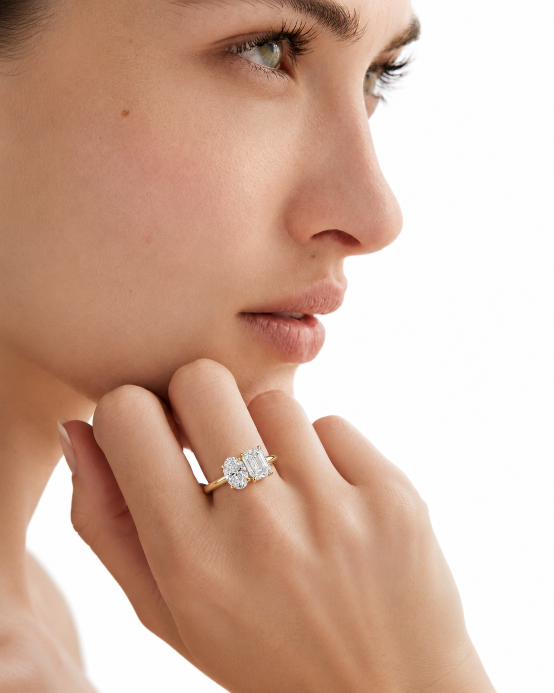 color_10K_YG, color_14K_YG &&A close-up of a woman's face and hand wearing a yellow gold ring with a four-stone diamond cluster setting, photographed against a clean white background.