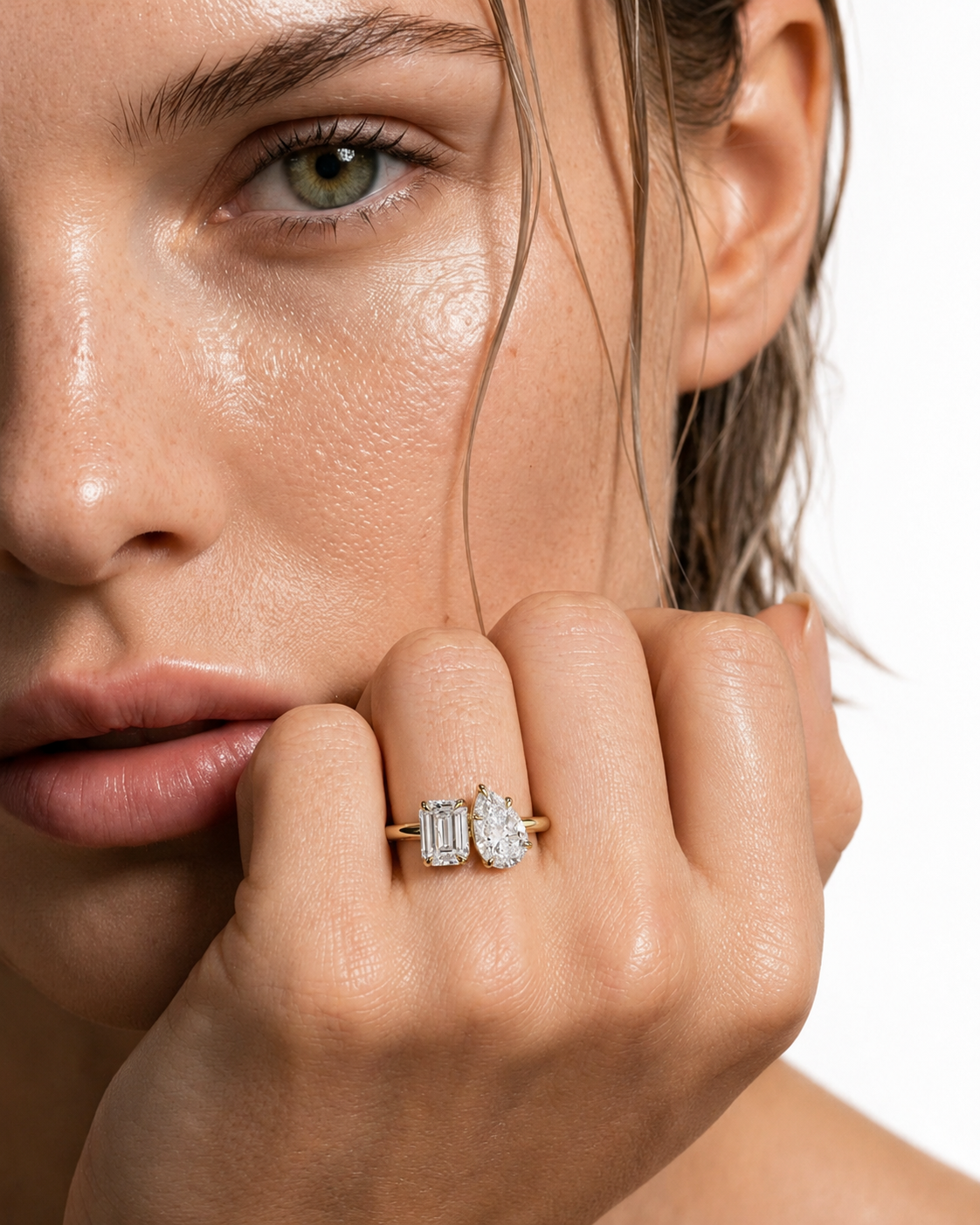 color_10K_YG, color_14K_YG &&A close-up of a woman's face and hand wearing a gold ring with two baguette-cut clear gemstones on a white background.