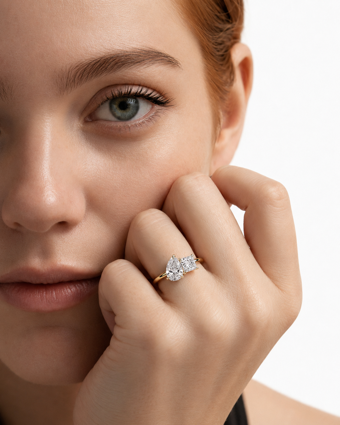color_10K_YG, color_14K_YG &&A close-up lifestyle shot of a woman with red hair wearing a gold ring with a pear-cut diamond on her finger, set against a clean white background.