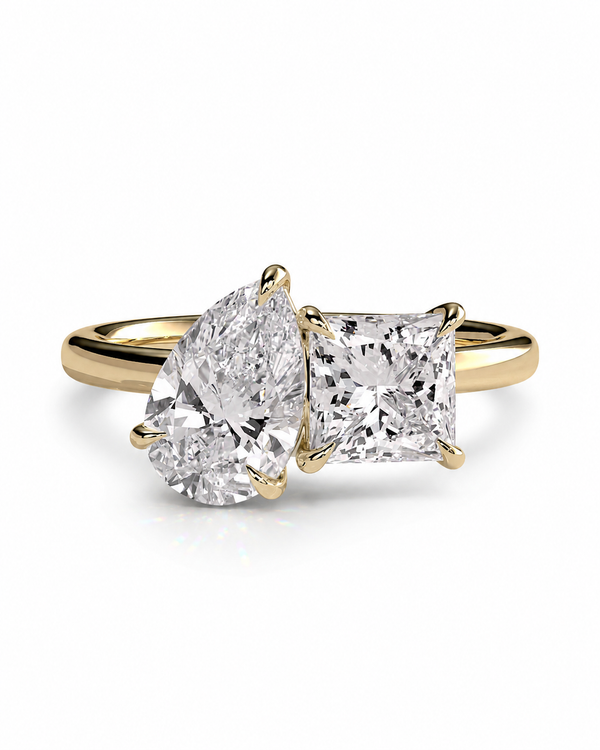 color_10K_YG, color_14K_YG &&A yellow gold ring featuring a pear-cut diamond on the left and a princess-cut diamond on the right, set on a polished gold band against a clean white background.