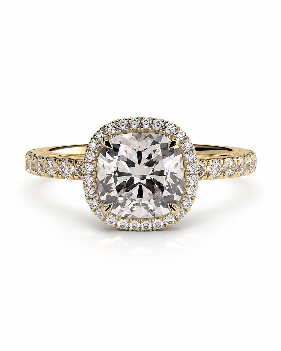color_10K_YG, color_14K_YG &&A yellow gold halo ring featuring a large cushion-cut center stone surrounded by a halo of small clear stones, with additional pavé stones along the shoulders, set against a plain white background.