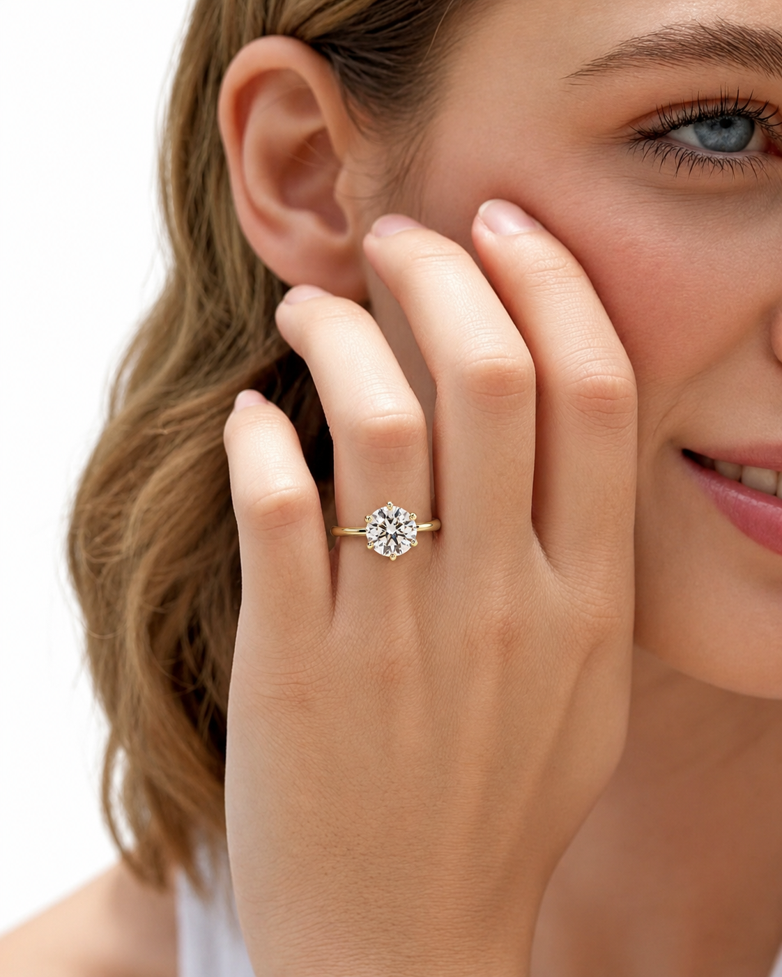 color_10K_YG, color_14K_YG &&A close-up lifestyle shot of a woman wearing a gold engagement ring with a round-cut clear gemstone on her finger, with her hand resting against her cheek against a clean white background.