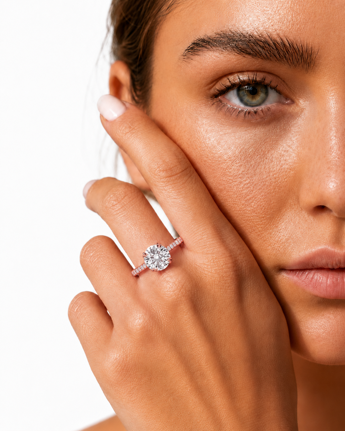 color_10K_RG, color_14K_RG &&
A close-up lifestyle shot of a woman wearing a sparkling diamond engagement ring on her finger, with her hand resting against her cheek against a clean white background.