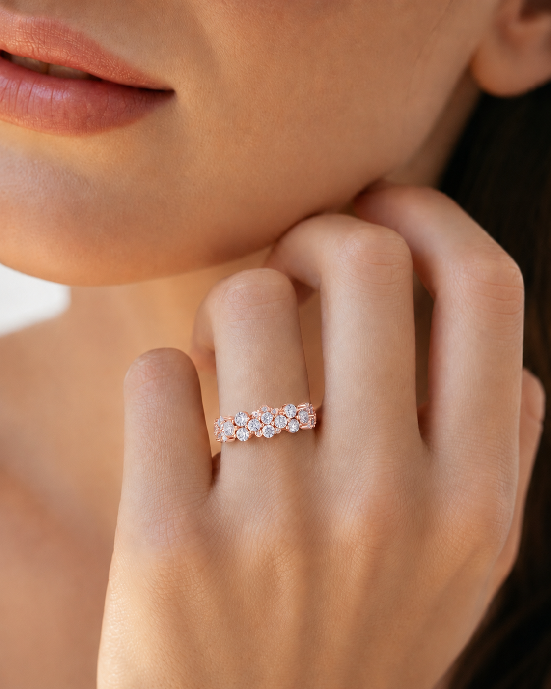 color_10K_RG, color_14K_RG &&	A close-up lifestyle shot of a model's hand wearing a delicate rose gold band ring set with small clear stones.