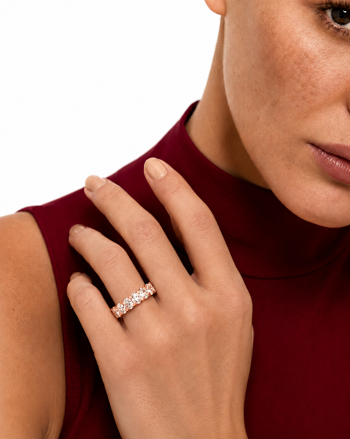 color_10K_RG, color_14K_RG &&	A close-up lifestyle shot of a woman wearing a rose gold eternity ring with small clear stones on her ring finger, paired with a deep burgundy mock neck top against a white background.