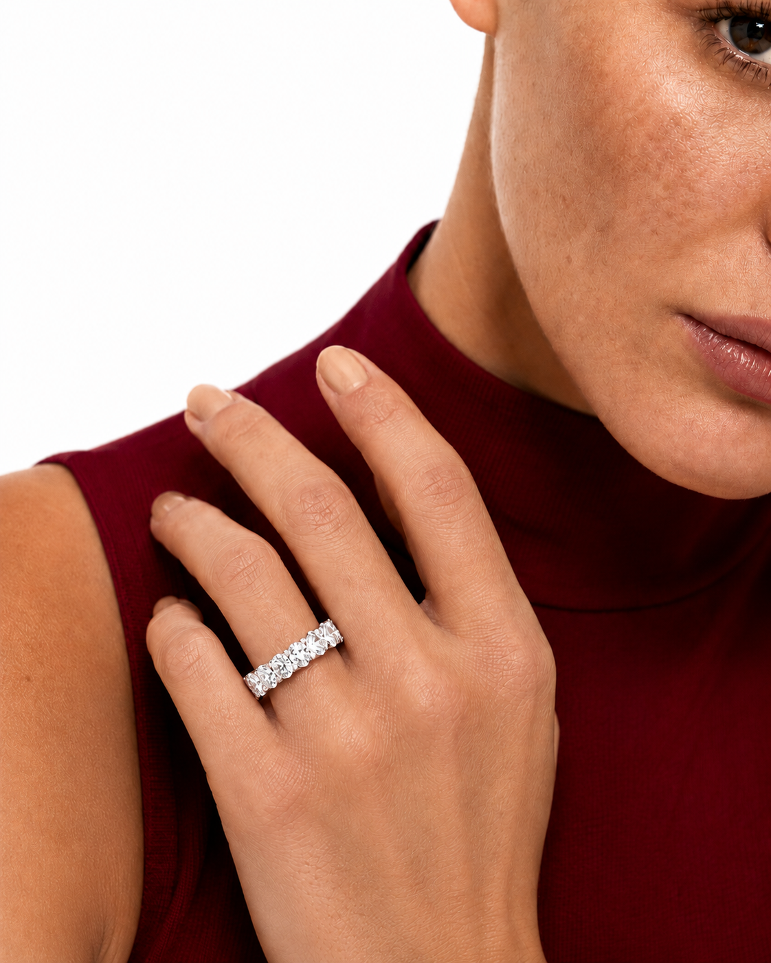 color_925_SIL,color_935_ARG,color_10K_WG, color_14K_WG &&	
A close-up of a woman wearing a diamond eternity ring on her finger, wearing a deep burgundy mock-neck top against a clean white background.