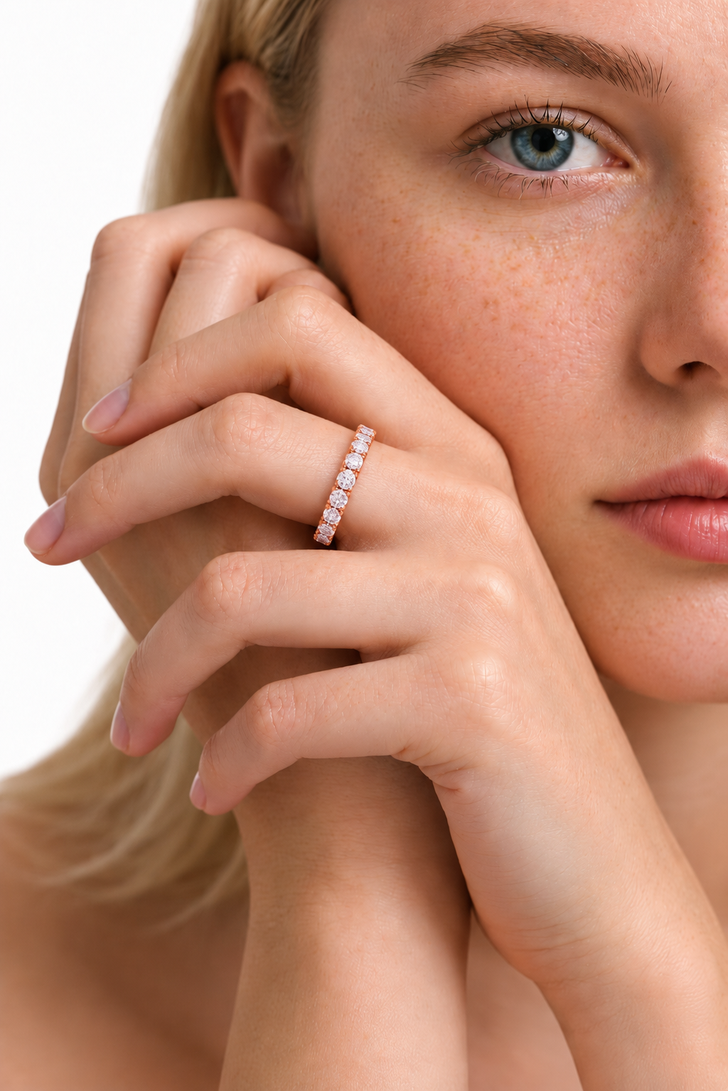 color_10K_RG, color_14K_RG &&	A close-up lifestyle shot of a woman wearing a delicate rose gold eternity ring set with small clear stones on her ring finger, against a clean white background.