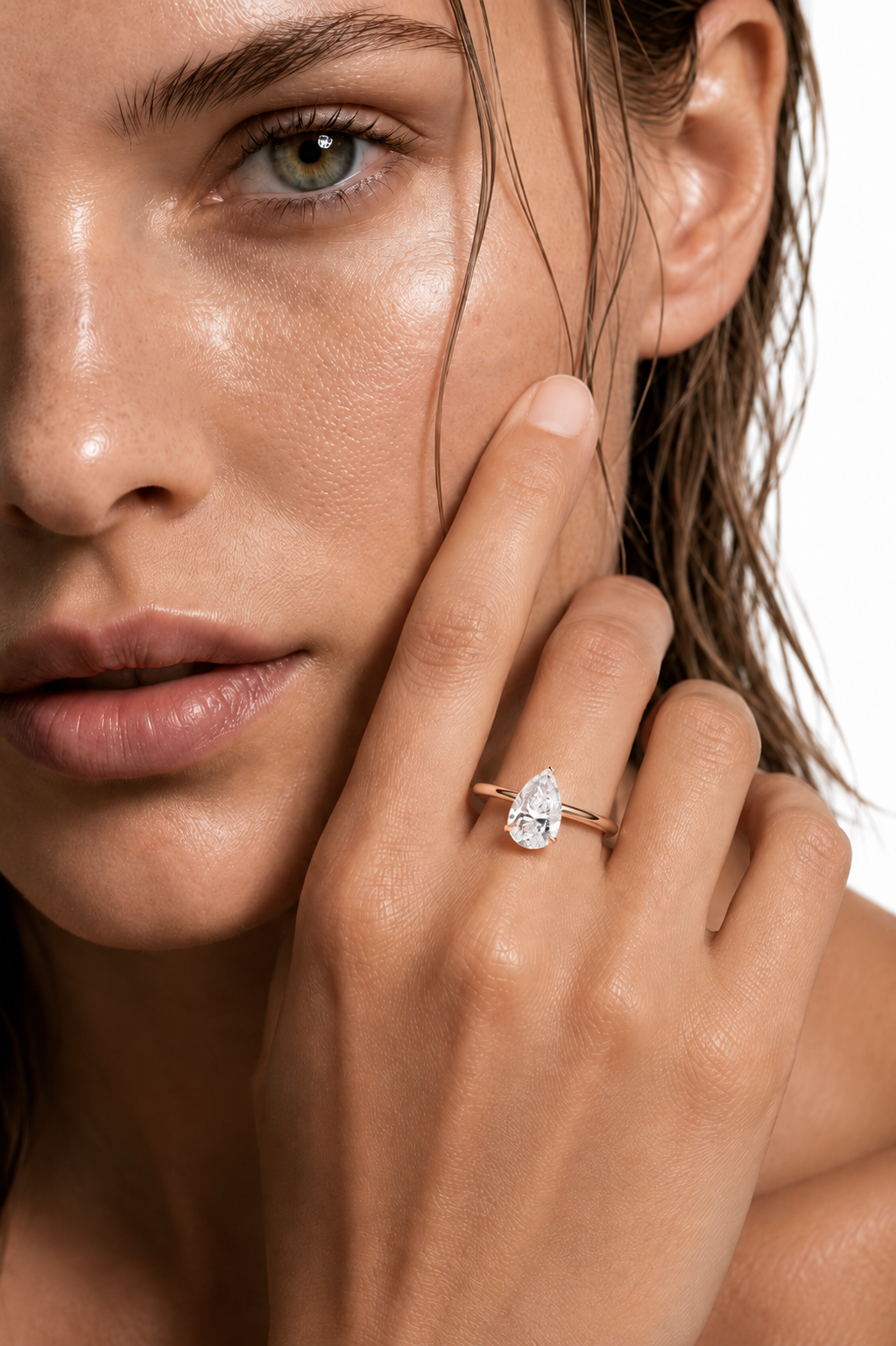 color_10K_RG, color_14K_RG &&
A close-up lifestyle shot of a model wearing a gold ring with a pear-cut clear gemstone on her finger, set against a clean white background.