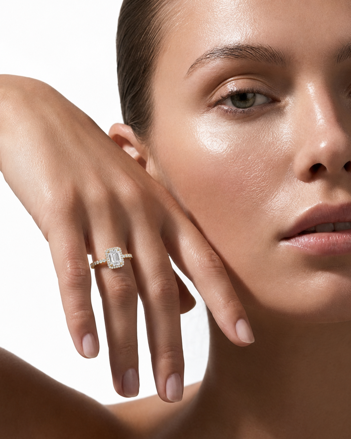 color_10K_YG, color_14K_YG &&A close-up lifestyle shot of a model wearing a yellow gold engagement ring with a rectangular emerald-cut diamond. The ring is shown on her finger as she rests her hand near her face against a clean white background.