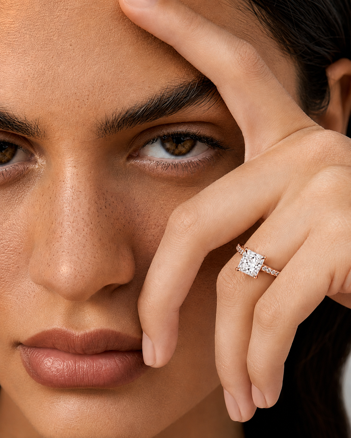color_10K_RG, color_14K_RG &&Close-up of a model's face and hand wearing a silver-toned ring with a square-cut clear gemstone.