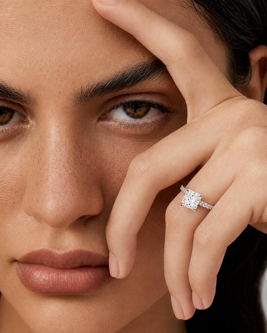 color_925_SIL,color_935_ARG,color_10K_WG, color_14K_WG &&A close-up lifestyle shot of a model wearing a diamond engagement ring on her ring finger. The ring features a cushion-cut diamond set in a silver-colored band.