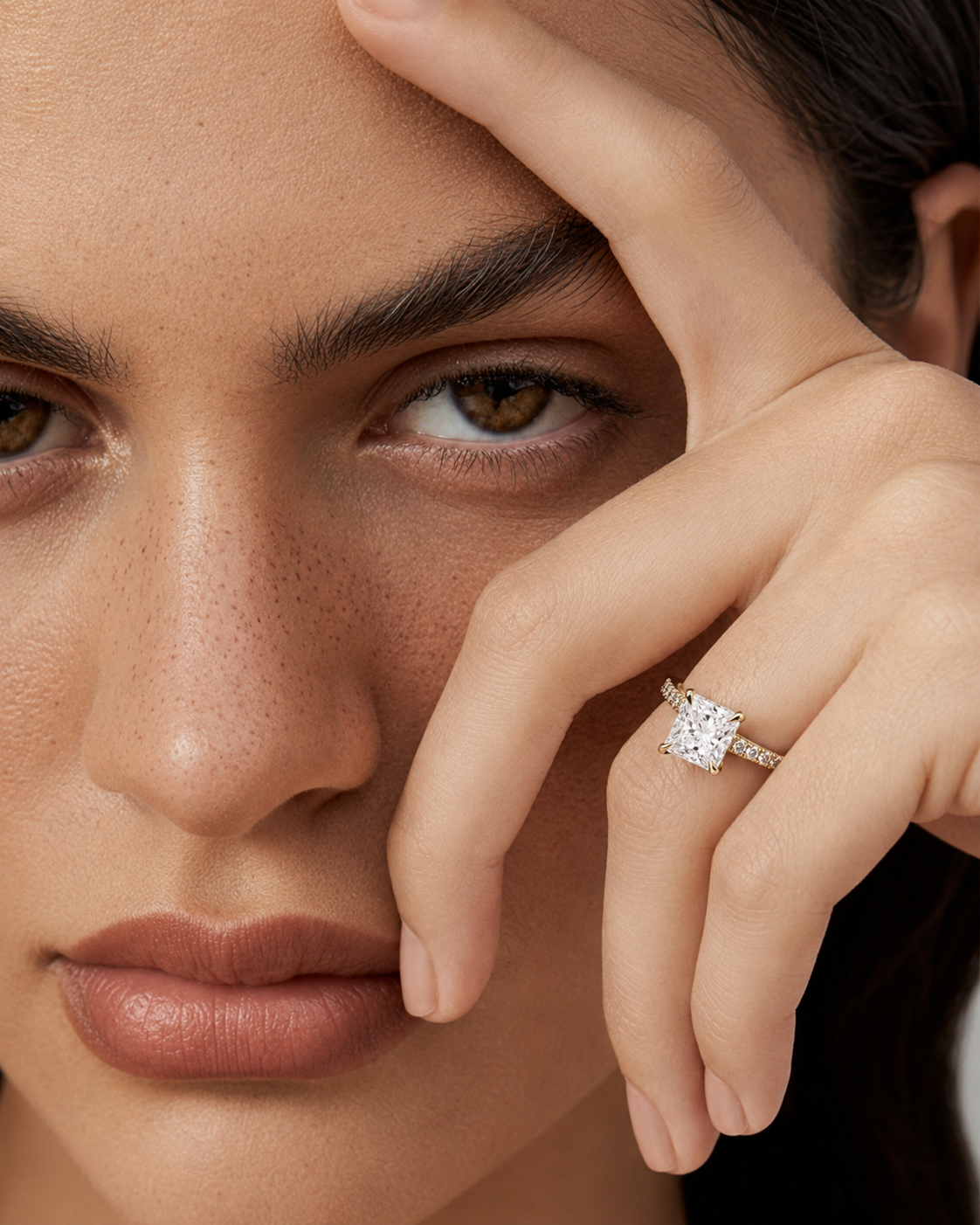 color_10K_YG, color_14K_YG &&A close-up of a model's face and hand wearing a silver-toned ring with a square-cut clear gemstone.