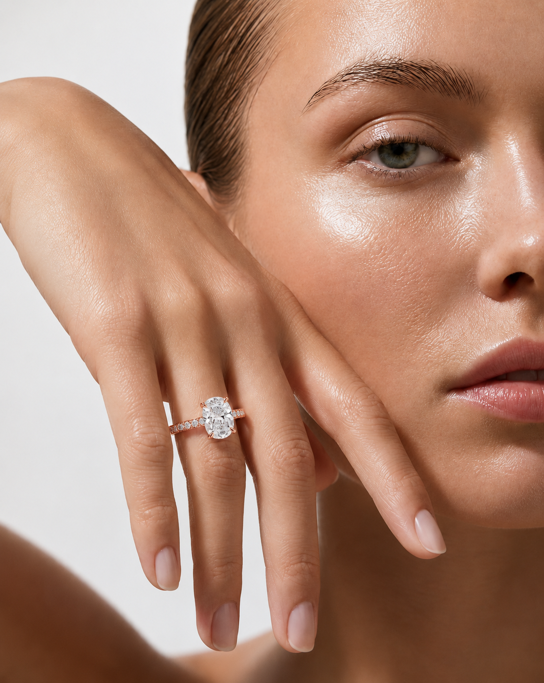 color_10K_RG, color_14K_RG &&A close-up lifestyle shot of a model wearing a diamond engagement ring on her finger, with her hand resting near her face against a clean, light background.