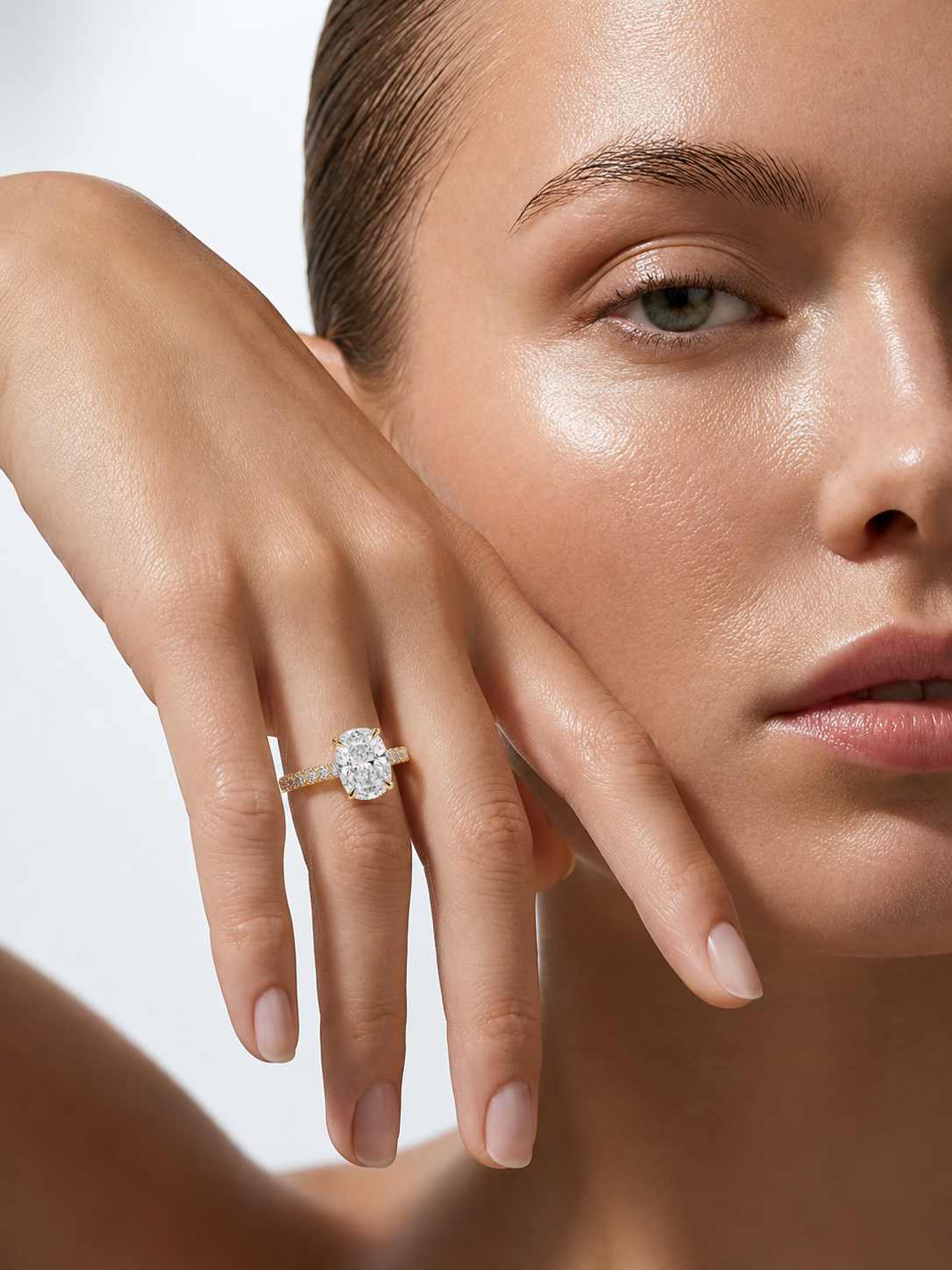 color_10K_YG, color_14K_YG &&A close-up lifestyle shot of a model wearing a yellow gold ring with a large oval-cut clear gemstone on her finger, set against a clean, light gray background.