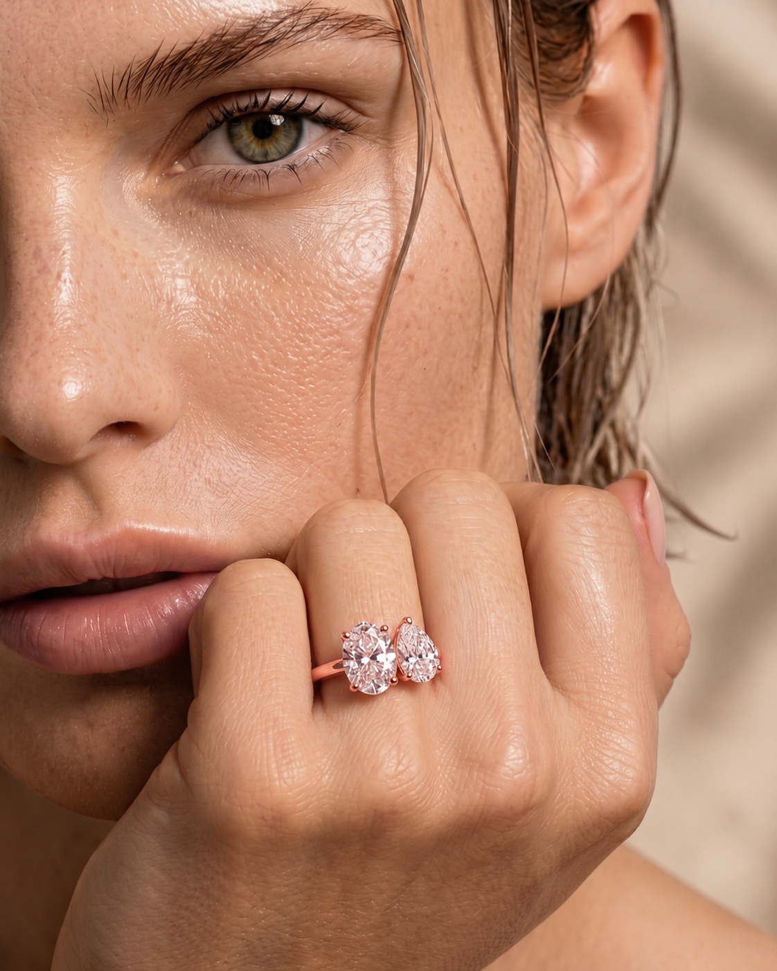 color_10K_RG, color_14K_RG &&A close-up lifestyle shot of a model wearing a rose gold ring with a cluster of clear gemstones on her finger, set against a soft beige background.