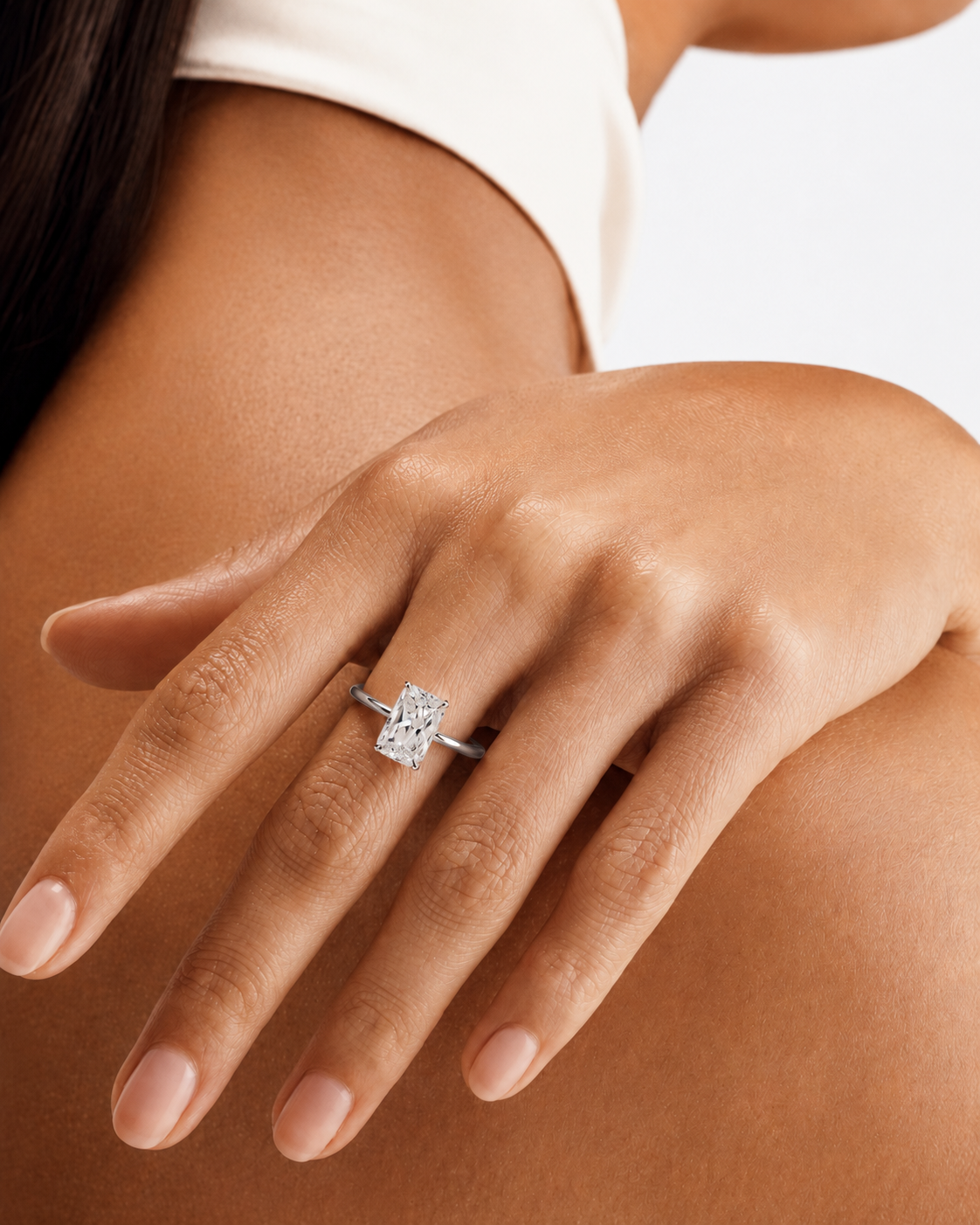 color_925_SIL,color_935_ARG,color_10K_WG, color_14K_WG &&A close-up of a woman's hand wearing a silver engagement ring with a rectangular clear center stone, set against her skin and a white top.