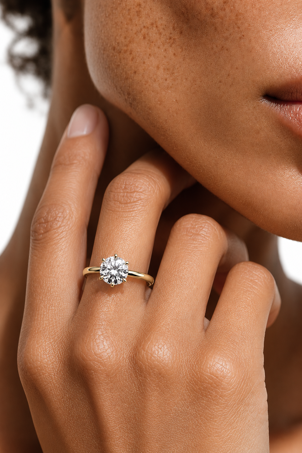 color_10K_YG, color_14K_YG &&A close-up of a model's hand wearing a yellow gold solitaire engagement ring with a round brilliant-cut diamond, set against a clean white background.