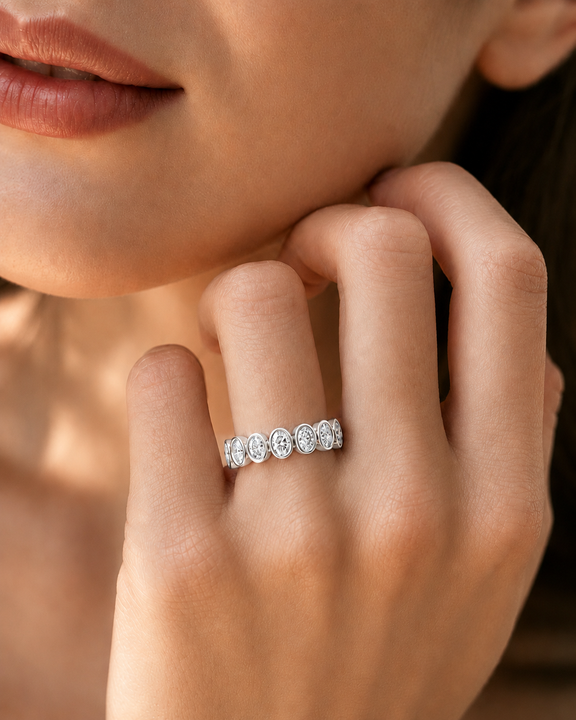 color_925_SIL,color_935_ARG,color_10K_WG, color_14K_WG &&	
A close-up lifestyle shot of a woman's hand wearing a silver band ring set with small round clear gemstones, against a warm, softly lit background.