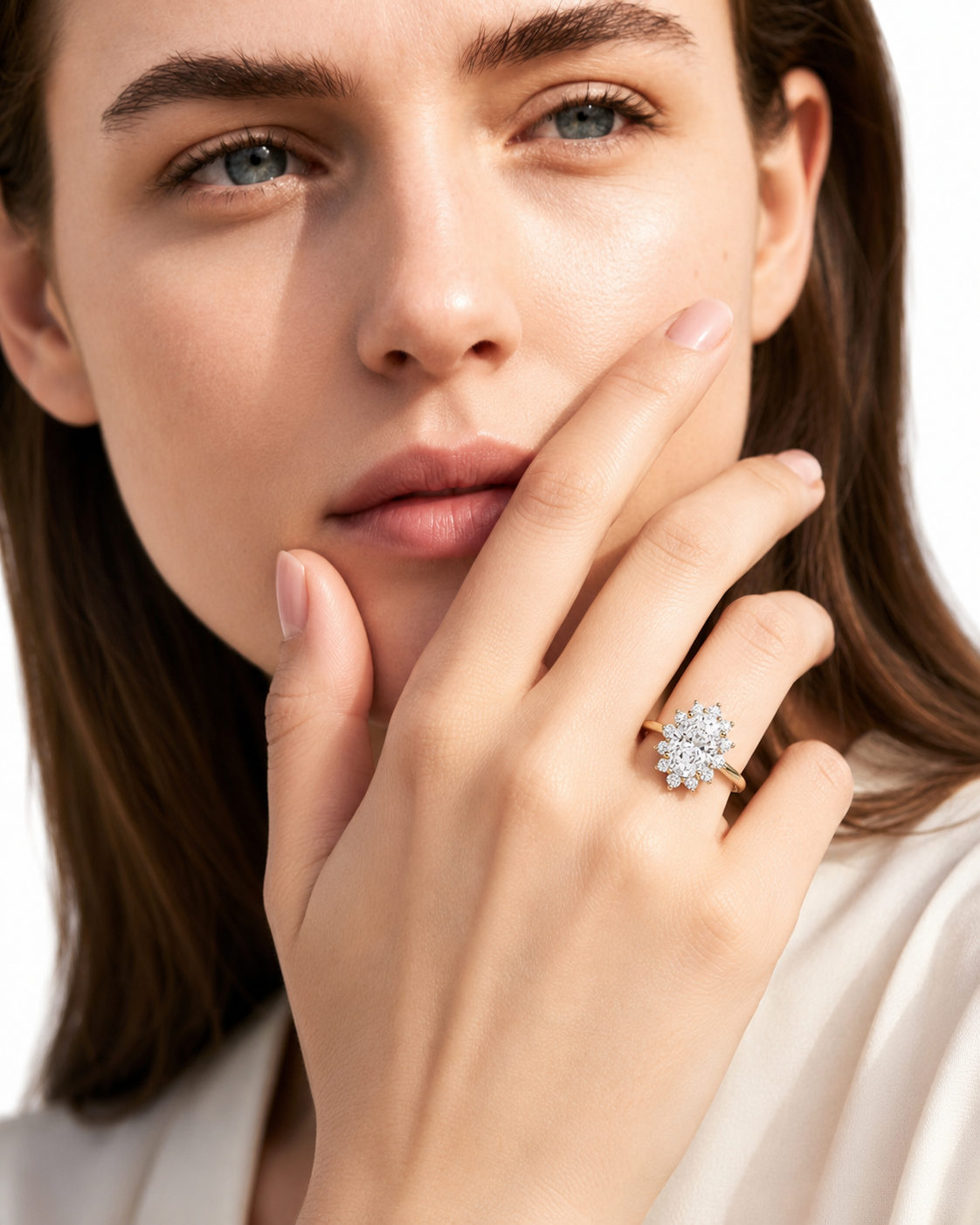 color_10K_YG, color_14K_YG &&A close-up lifestyle shot of a woman wearing a yellow gold ring with a clear diamond cluster on her ring finger, set against a clean white background.