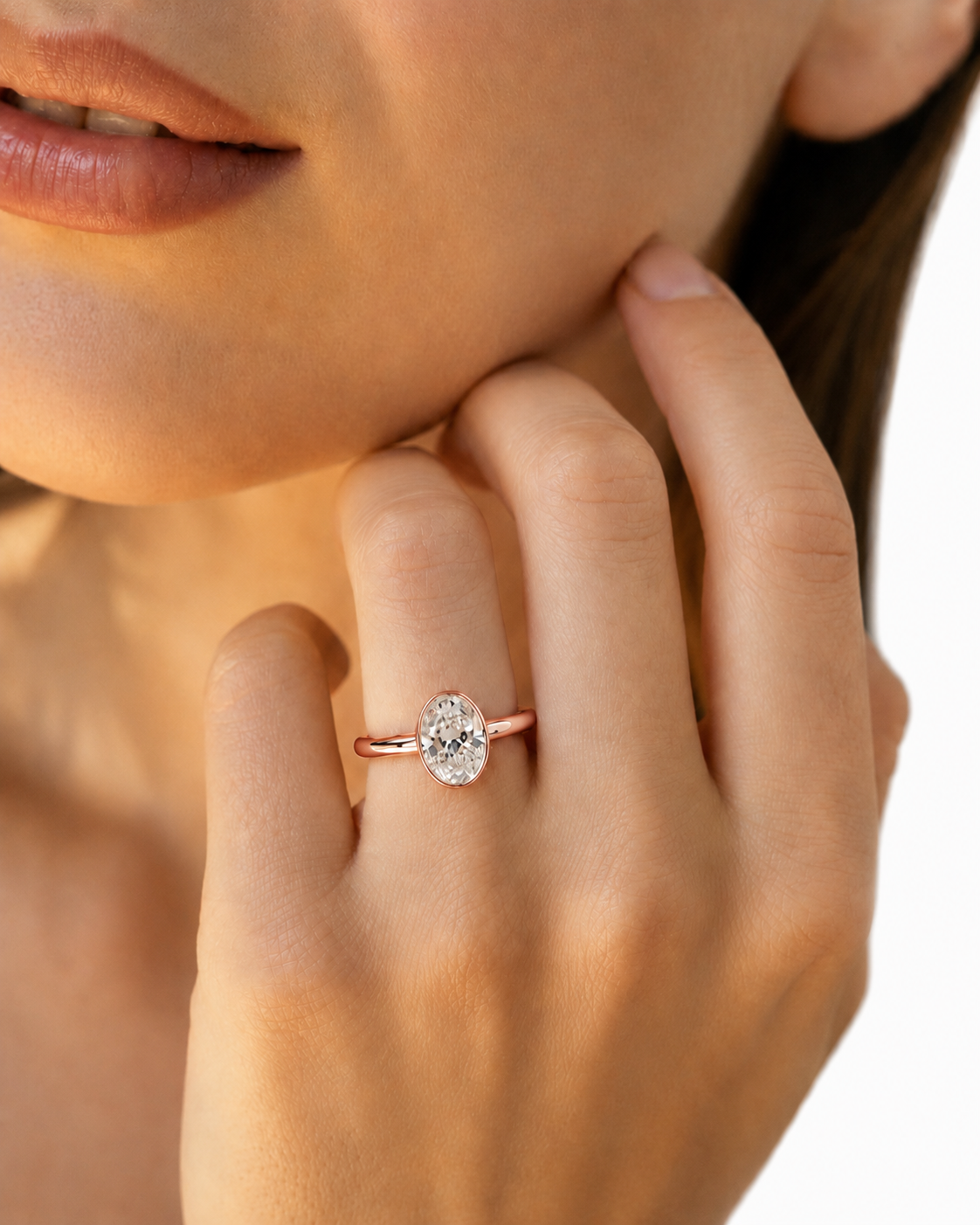 color_10K_RG, color_14K_RG &&A close-up lifestyle shot of a woman wearing a rose gold engagement ring with a round-cut clear gemstone on her finger, set against a clean white background.