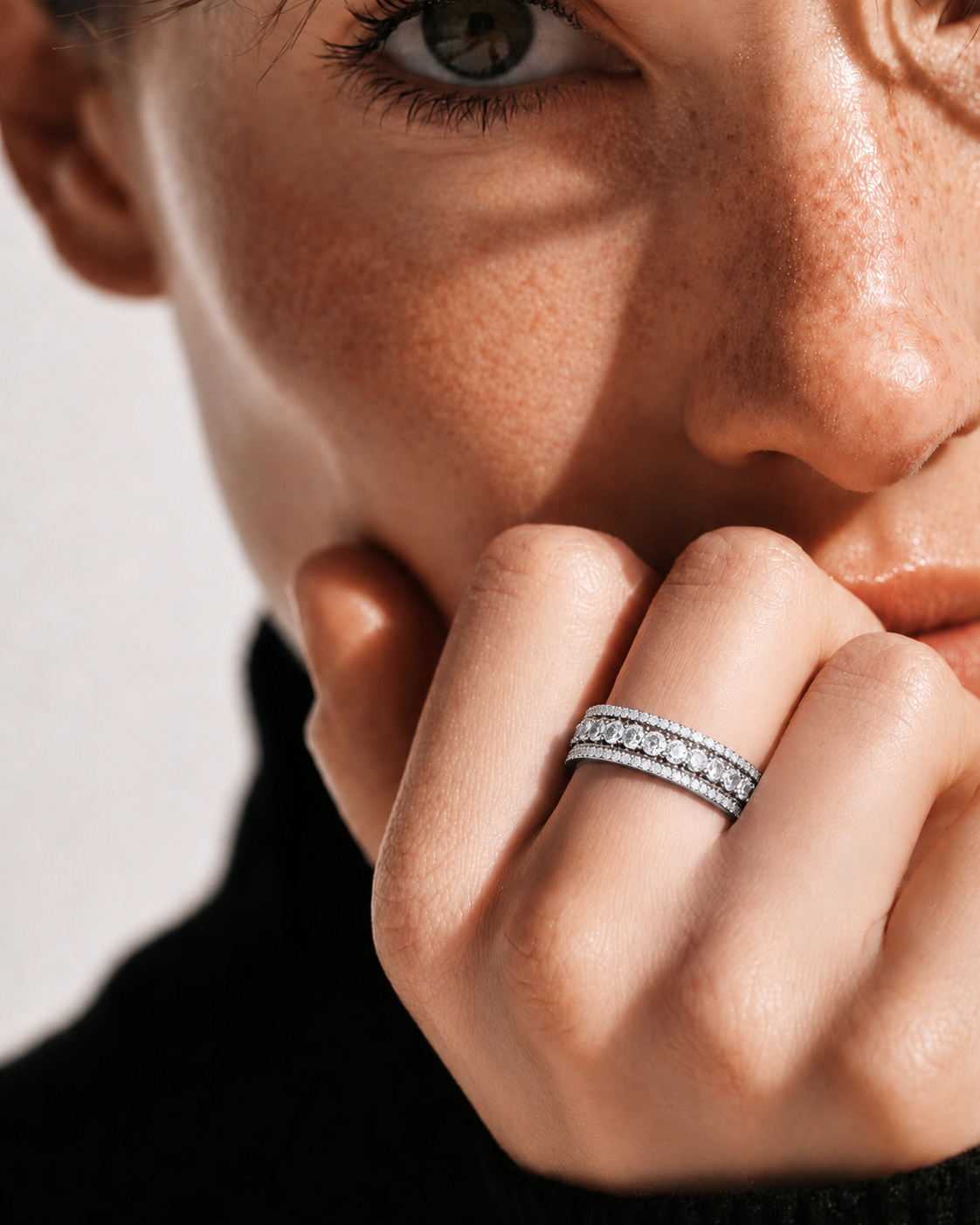 color_925_SIL,color_935_ARG,color_10K_WG, color_14K_WG &&	
A close-up lifestyle shot of a model wearing a silver double-band ring set with small clear stones. The image features dramatic, high-contrast warm lighting and a clean, neutral background.