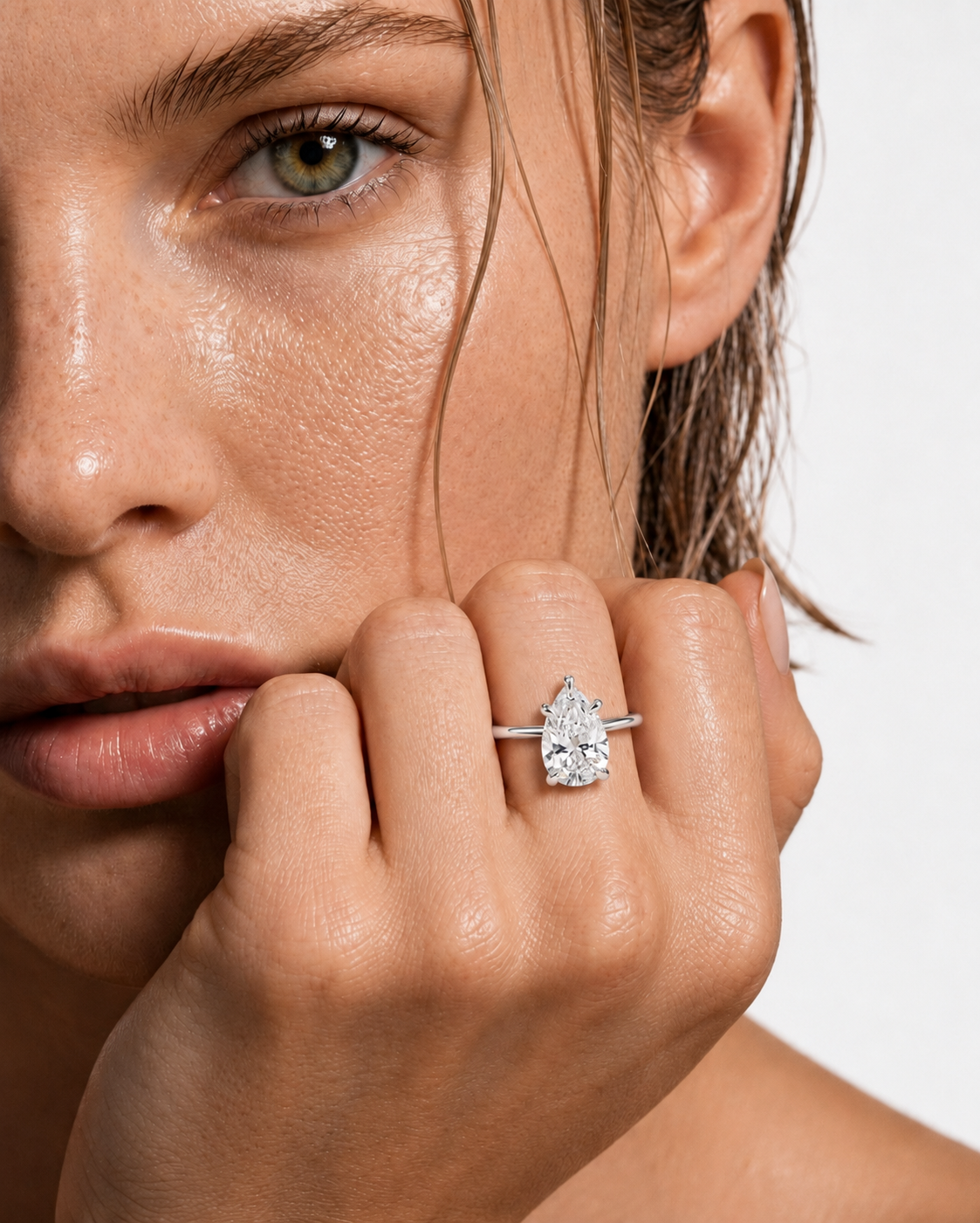 color_925_SIL,color_935_ARG,color_10K_WG, color_14K_WG &&A close-up lifestyle shot of a model wearing a silver ring with a pear-cut clear gemstone on her finger, set against a clean white background.