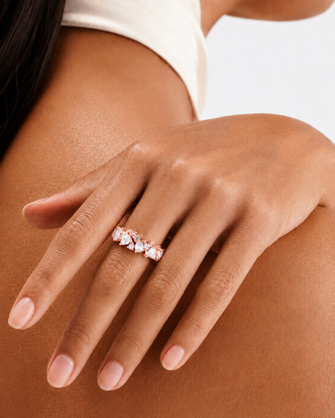 color_10K_RG, color_14K_RG &&	A close-up of a woman's hand wearing a rose gold ring with a row of clear marquise-cut gemstones, set against her bare shoulder and upper arm.