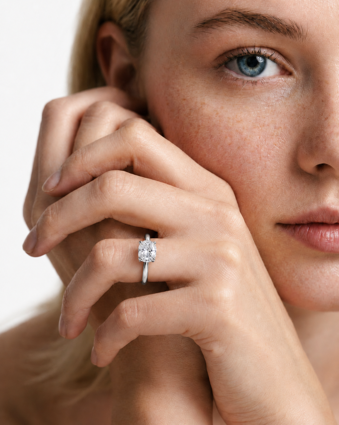 color_925_SIL,color_935_ARG,color_10K_WG, color_14K_WG &&A close-up lifestyle shot of a woman wearing a silver-toned ring with a round-cut clear gemstone on her finger, with her hand resting near her face against a clean white background.