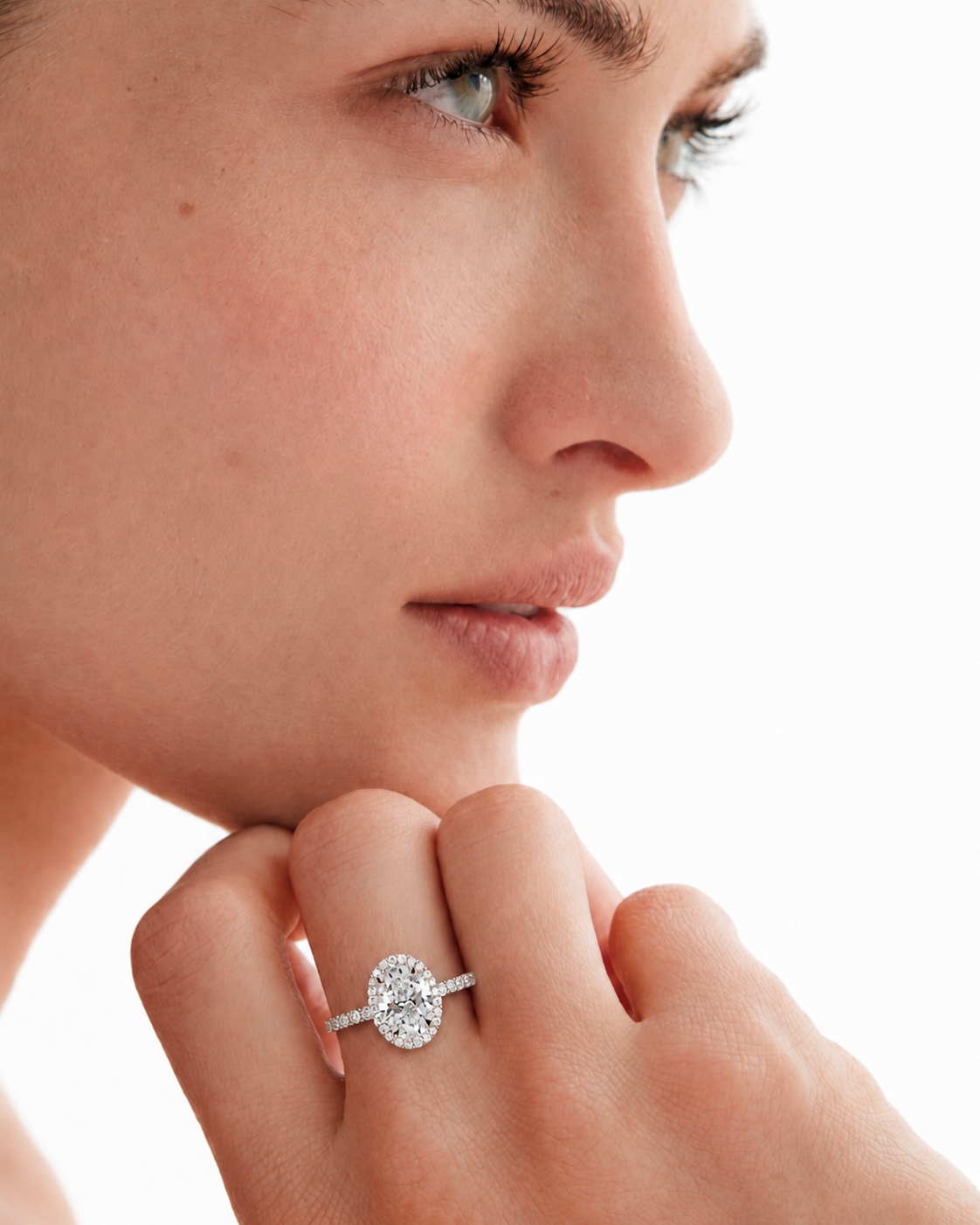 color_925_SIL,color_935_ARG,color_10K_WG, color_14K_WG &&A close-up side profile of a woman resting her chin on her hand, wearing a silver-toned ring with a round-cut clear gemstone.