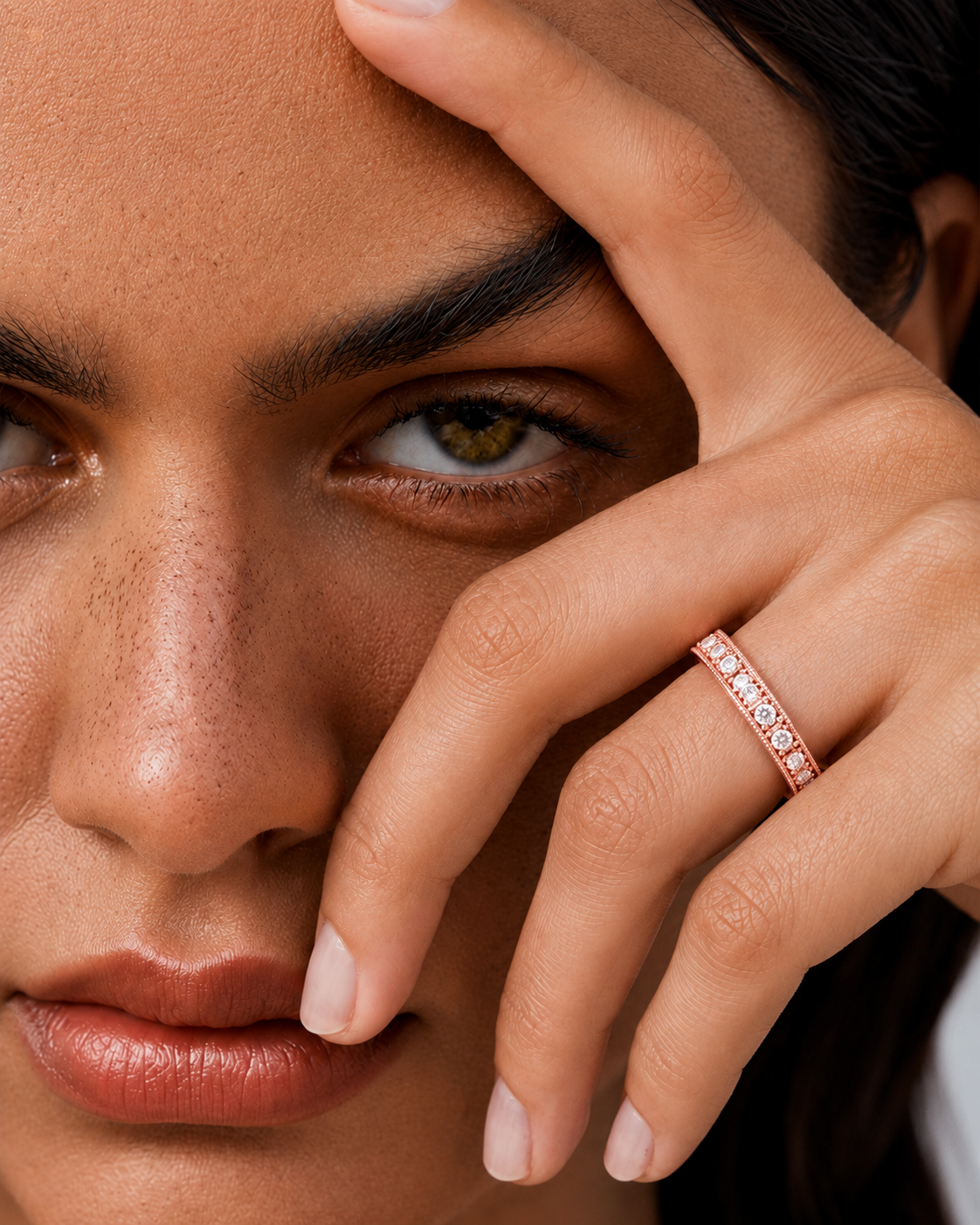 color_10K_RG, color_14K_RG &&	A close-up lifestyle shot of a model wearing a delicate rose gold band ring with small clear stones, resting her hand on her cheek.