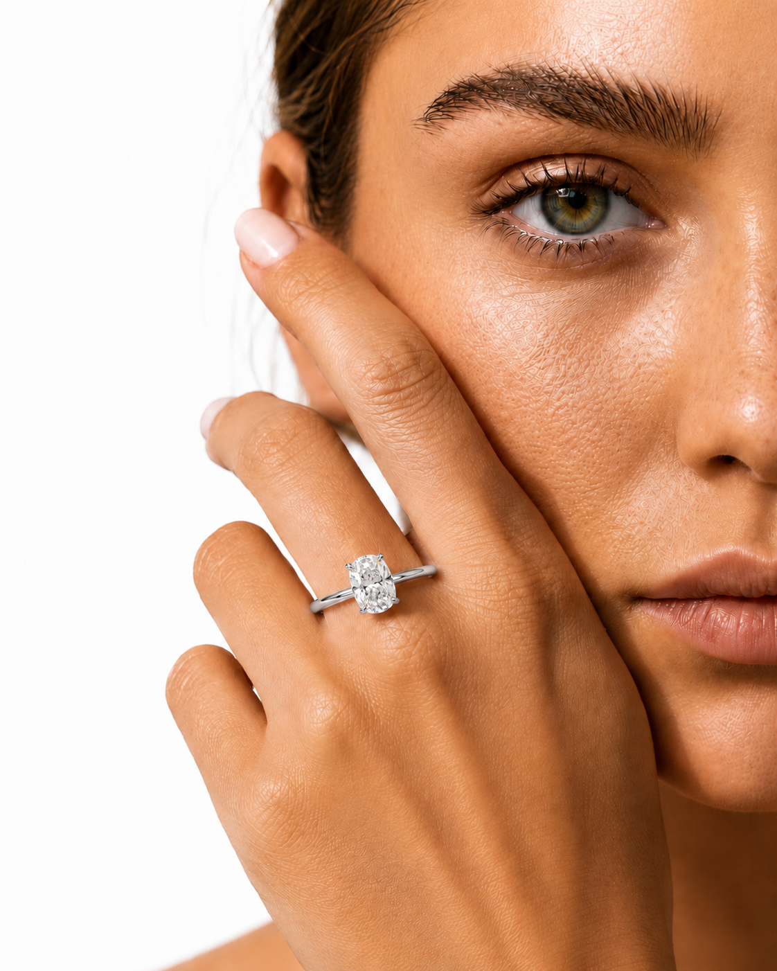 color_925_SIL,color_935_ARG,color_10K_WG, color_14K_WG &&A close-up lifestyle shot of a woman wearing a silver-toned engagement ring with a round-cut clear gemstone on her finger, with her hand resting against her cheek against a white background.