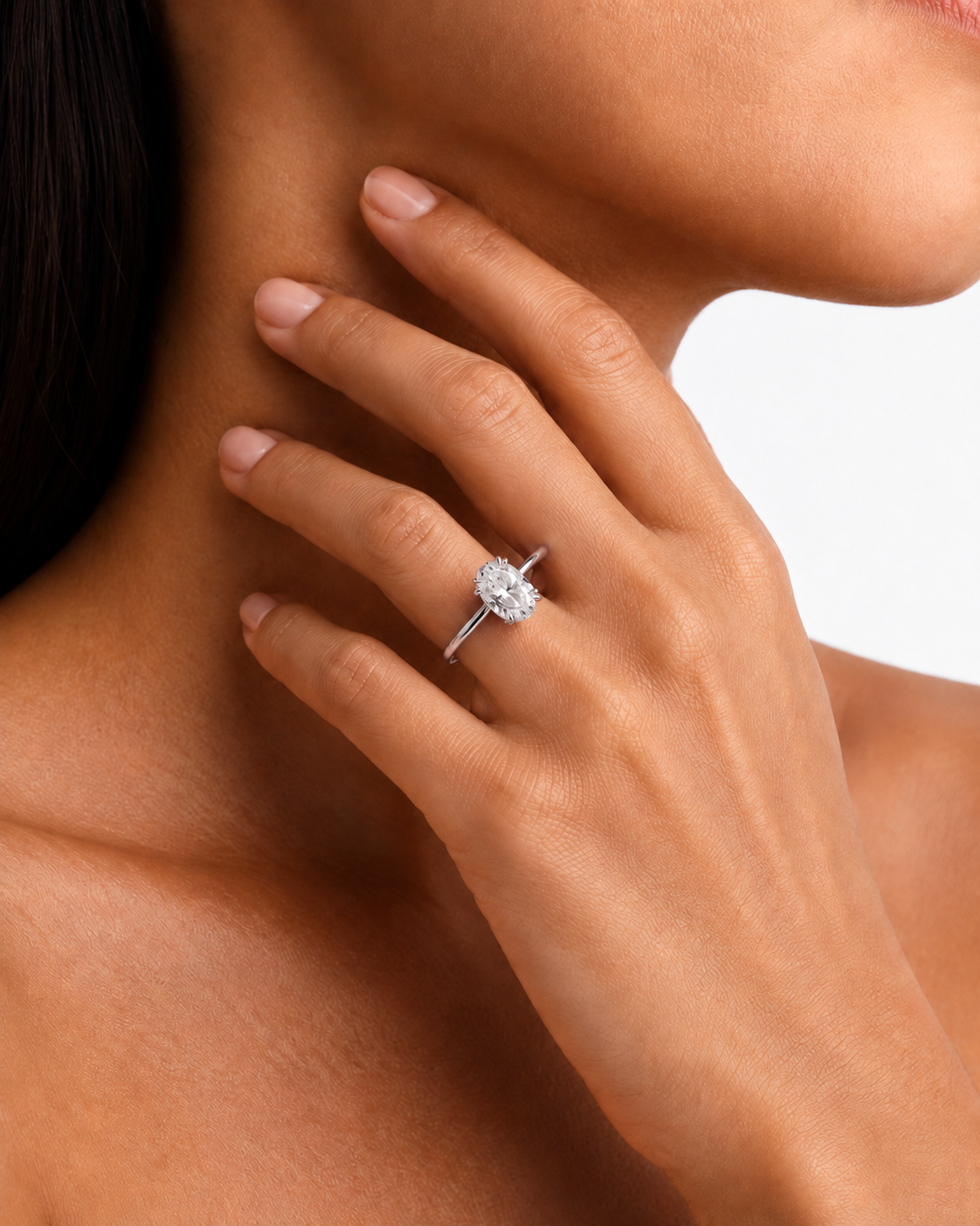 color_925_SIL,color_935_ARG,color_10K_WG, color_14K_WG &&A close-up lifestyle shot of a model's hand resting on her neck, wearing a silver-toned diamond engagement ring.