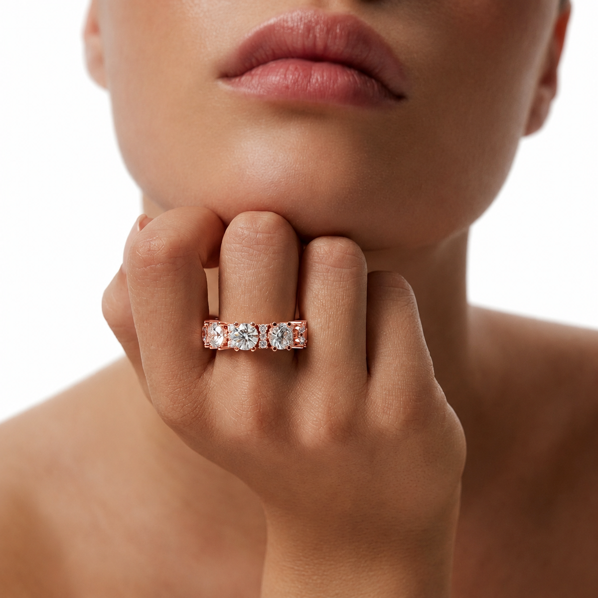 color_10K_RG, color_14K_RG &&	A close-up lifestyle shot of a model's hand and lower face wearing a yellow gold eternity ring set with clear round-cut gemstones.