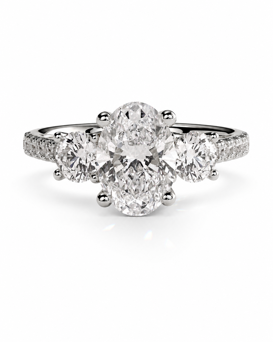 color_925_SIL,color_935_ARG,color_10K_WG, color_14K_WG &&A three-stone diamond engagement ring with a silver-toned band, featuring a large oval center diamond flanked by two round diamonds, set against a clean white background.