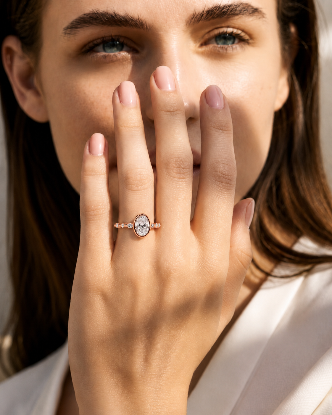 color_10K_RG, color_14K_RG &&A close-up lifestyle shot of a woman wearing a rose gold ring with a marquise-cut clear gemstone and small side stones, holding her hand near her face.