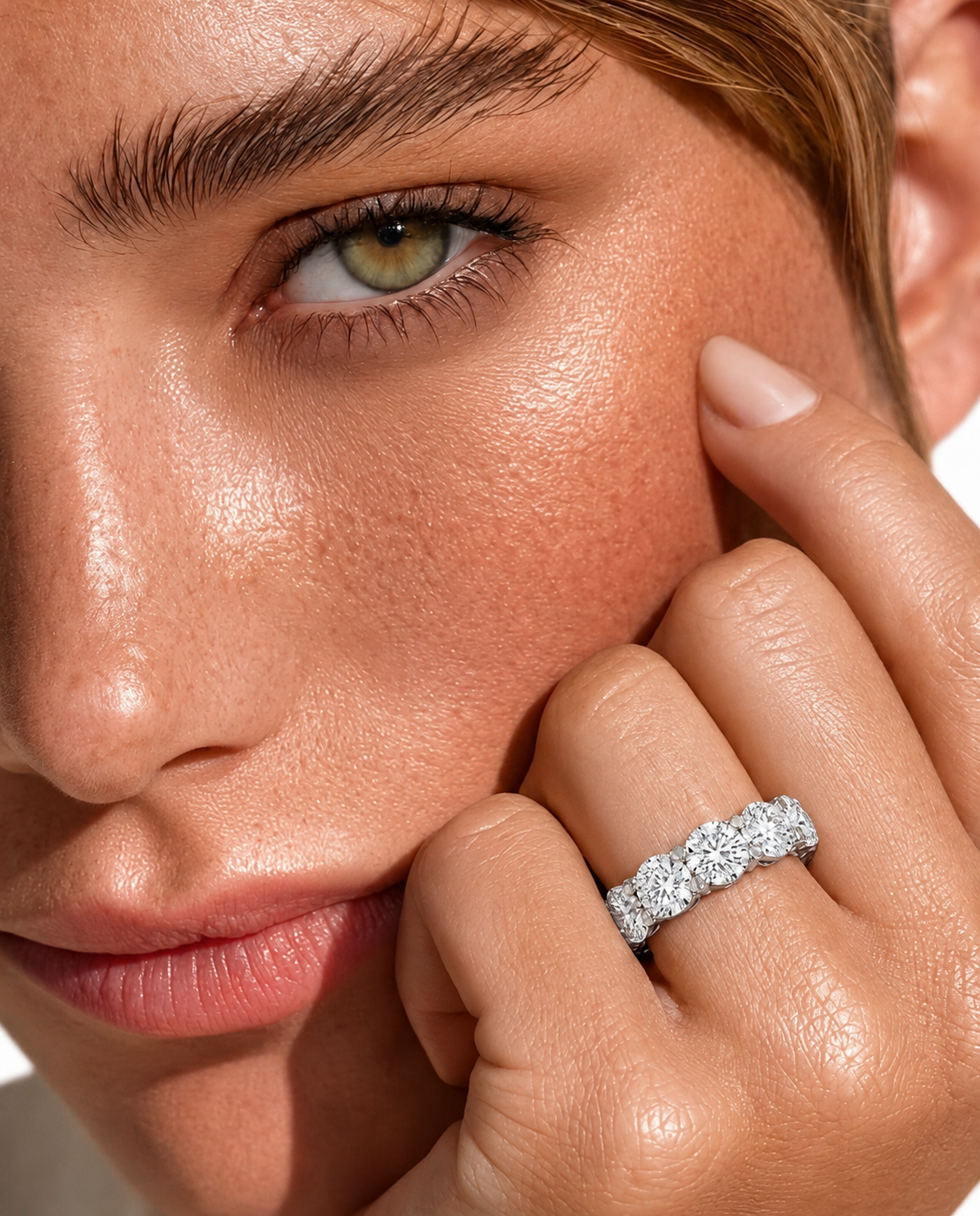 color_925_SIL,color_935_ARG,color_10K_WG, color_14K_WG &&	
Close-up of a model's face and hand wearing a sparkling diamond eternity ring on her ring finger.